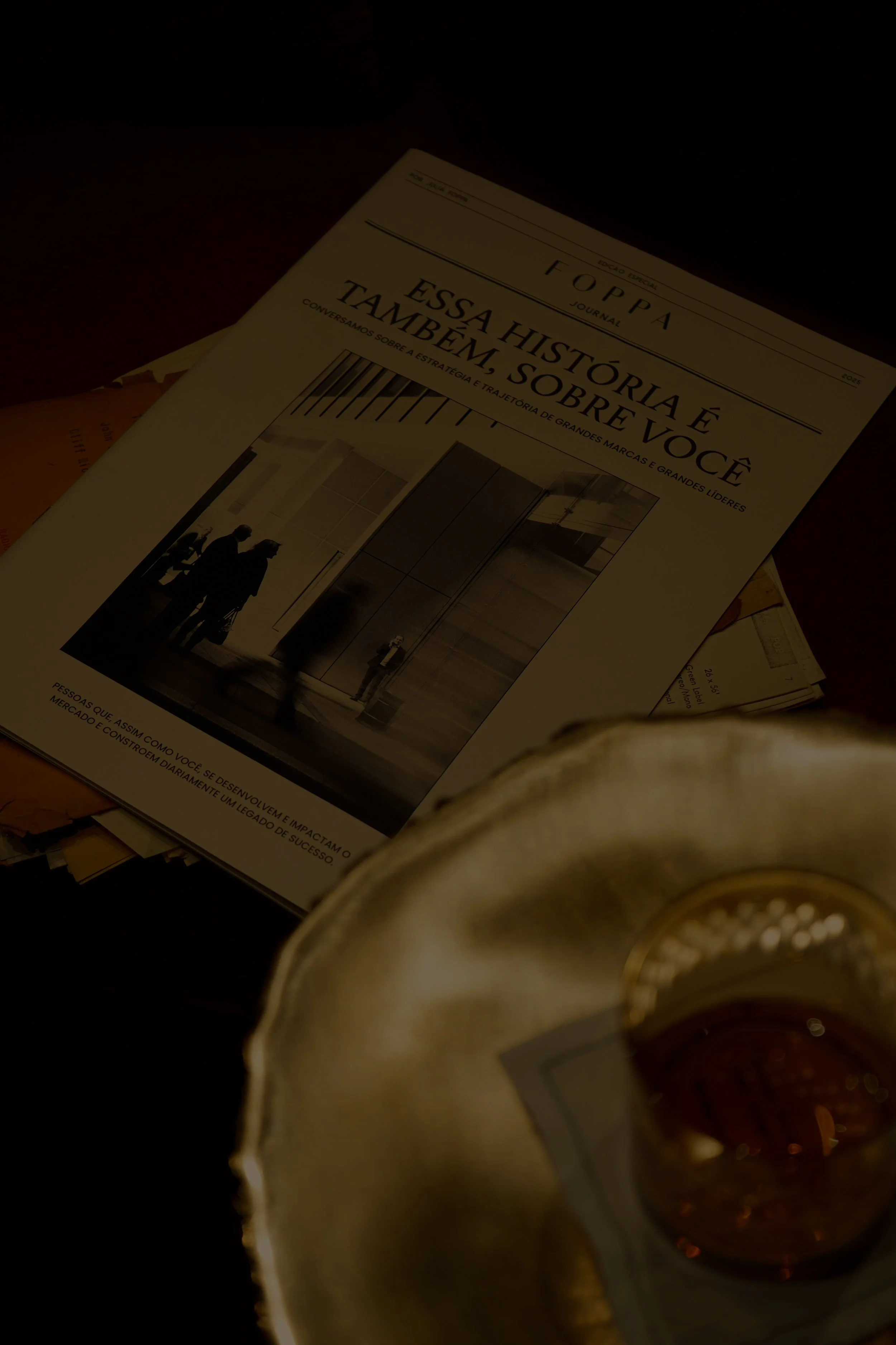 Revista Foppé com título que diz 'Essa história é também sobre você', com uma foto de duas pessoas em um ambiente moderno, vista parcialmente ao lado de um copo com bebida em um prato