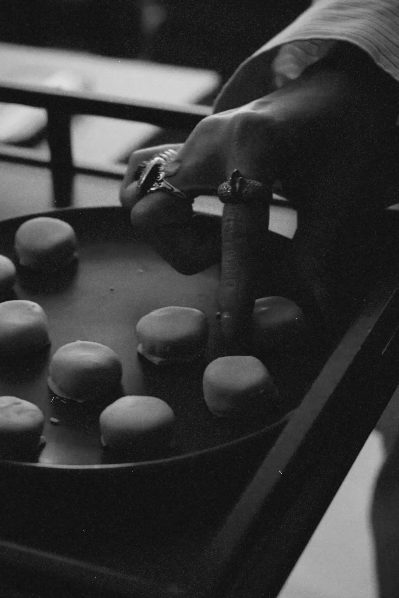 Pessoa jogando biribol, uma bolinha de gude, em uma mesa com várias bolinhas, em uma imagem em preto e branco.