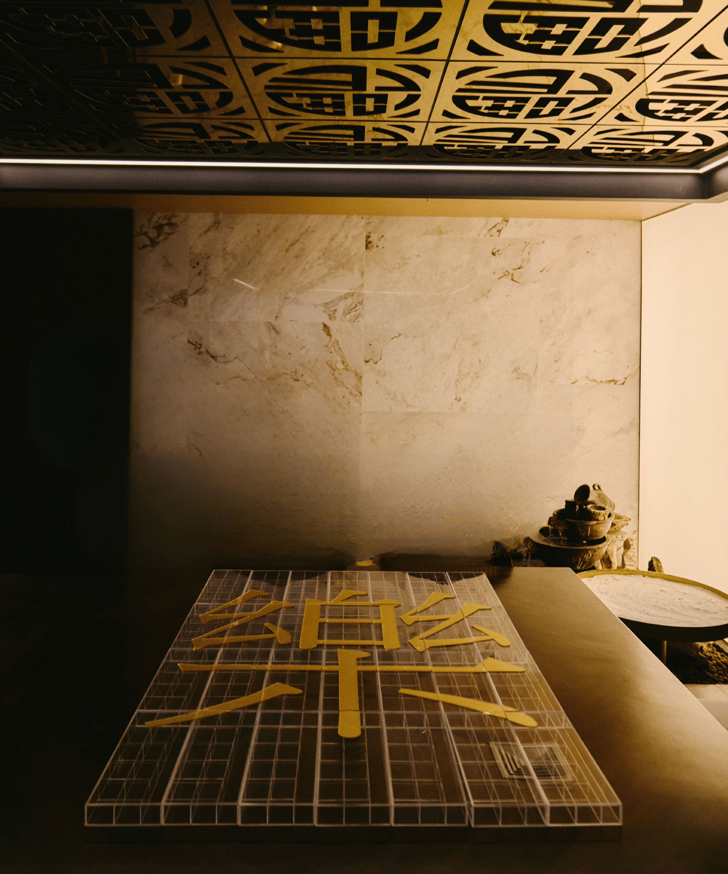 Imagem de uma superfície com várias peças de material amarelo e uma moldura de grade, ao fundo uma parede de mármore e objetos decorativos em uma mesa.