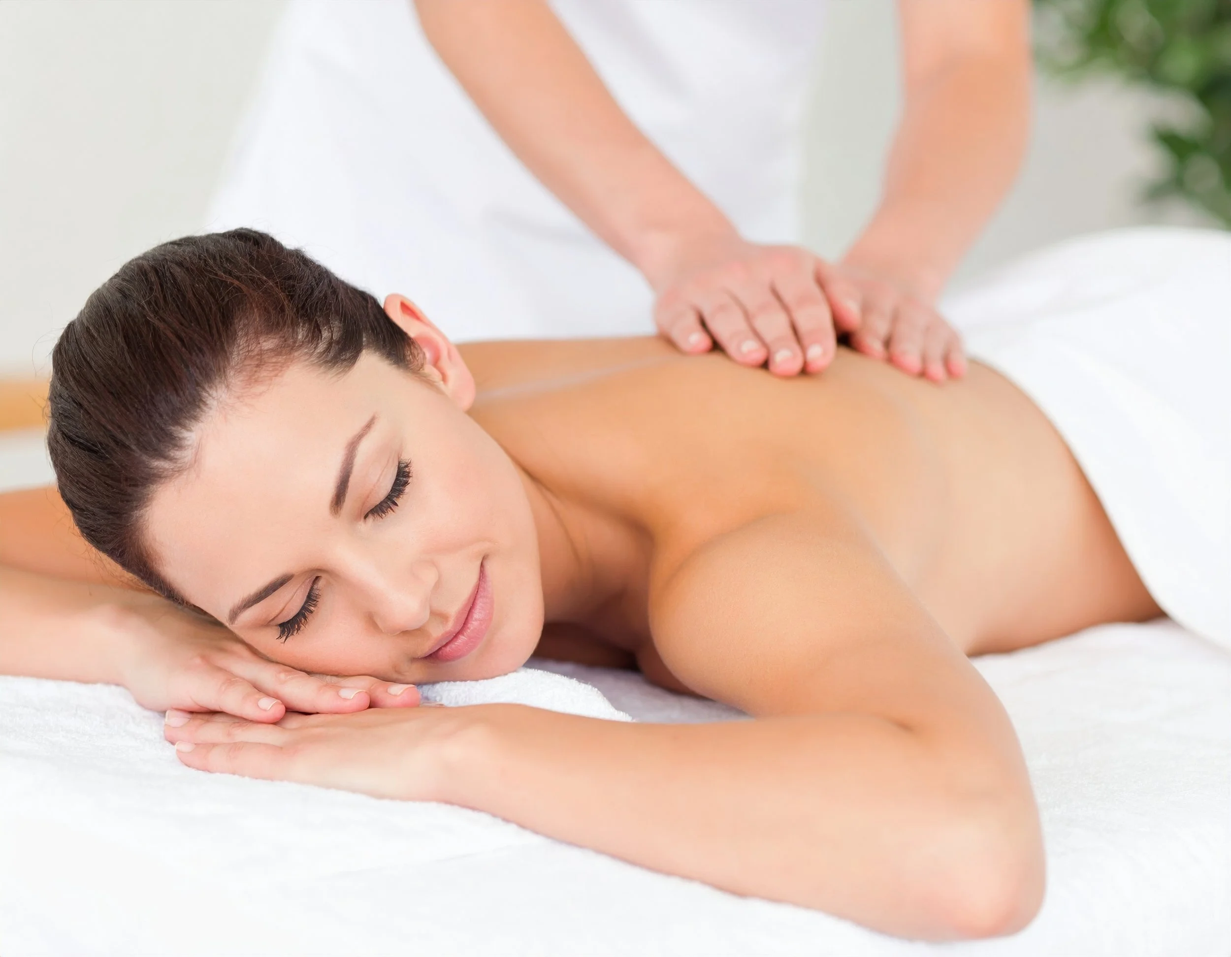 A woman receives a back massage while lying on her stomach with eyes closed, in a spa setting.