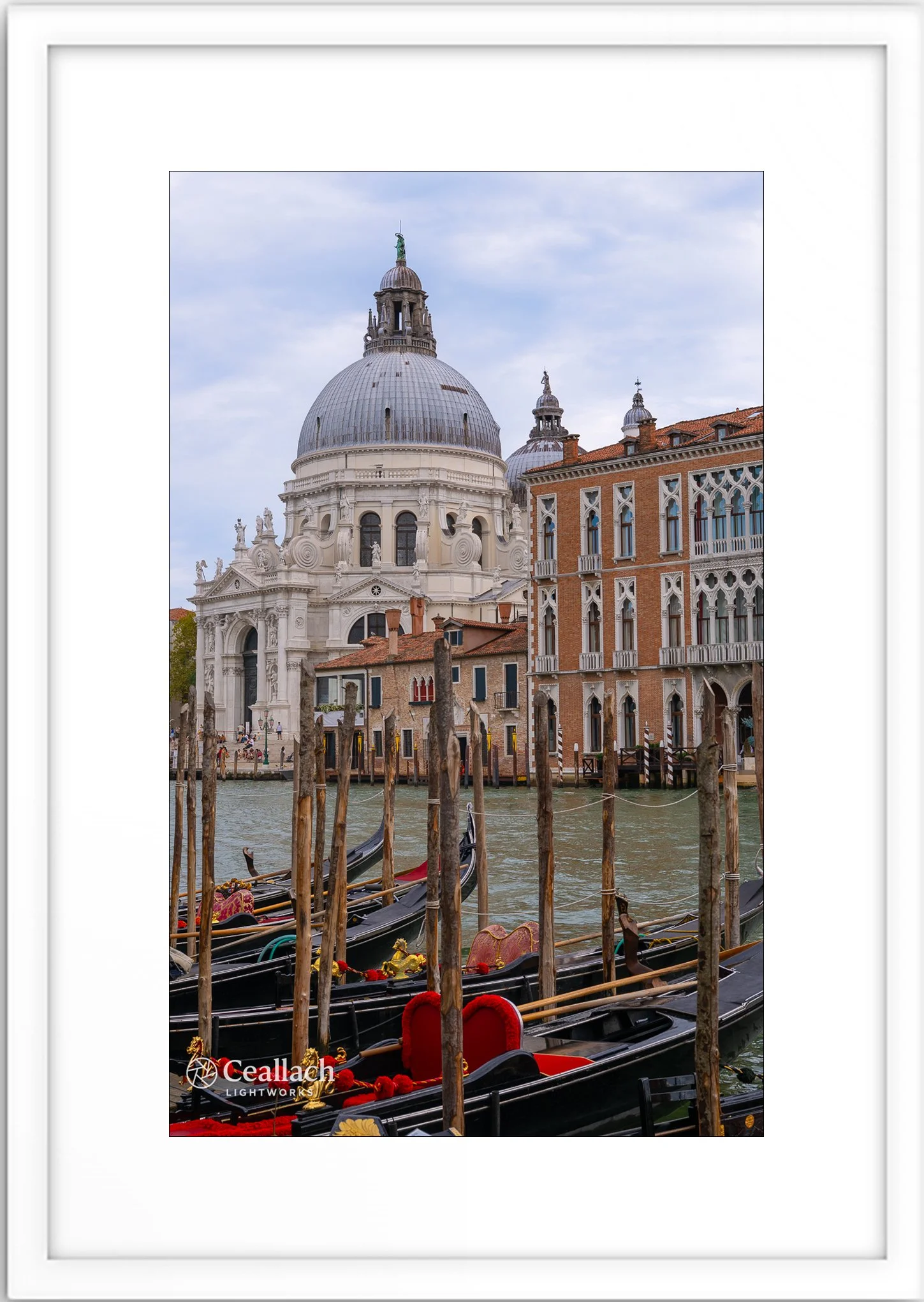 Gondolas floating on a canal in Venice with historic buildings and a large domed church in the background on a cloudy day.
