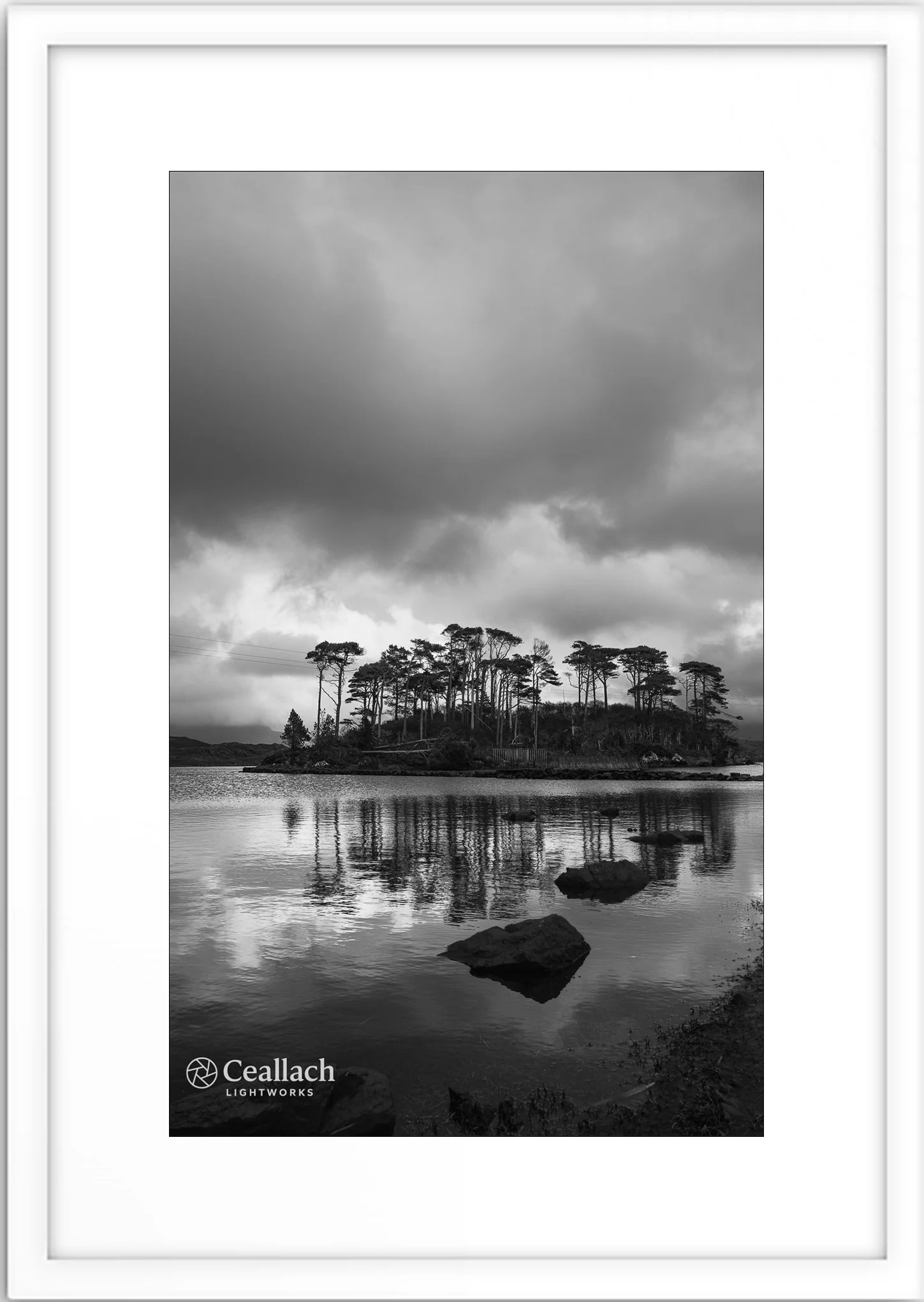 A black and white photograph of a small island with tall trees, surrounded by water with rocks, under a cloudy sky. Logo of Ceallach Lightworks in the bottom left corner.