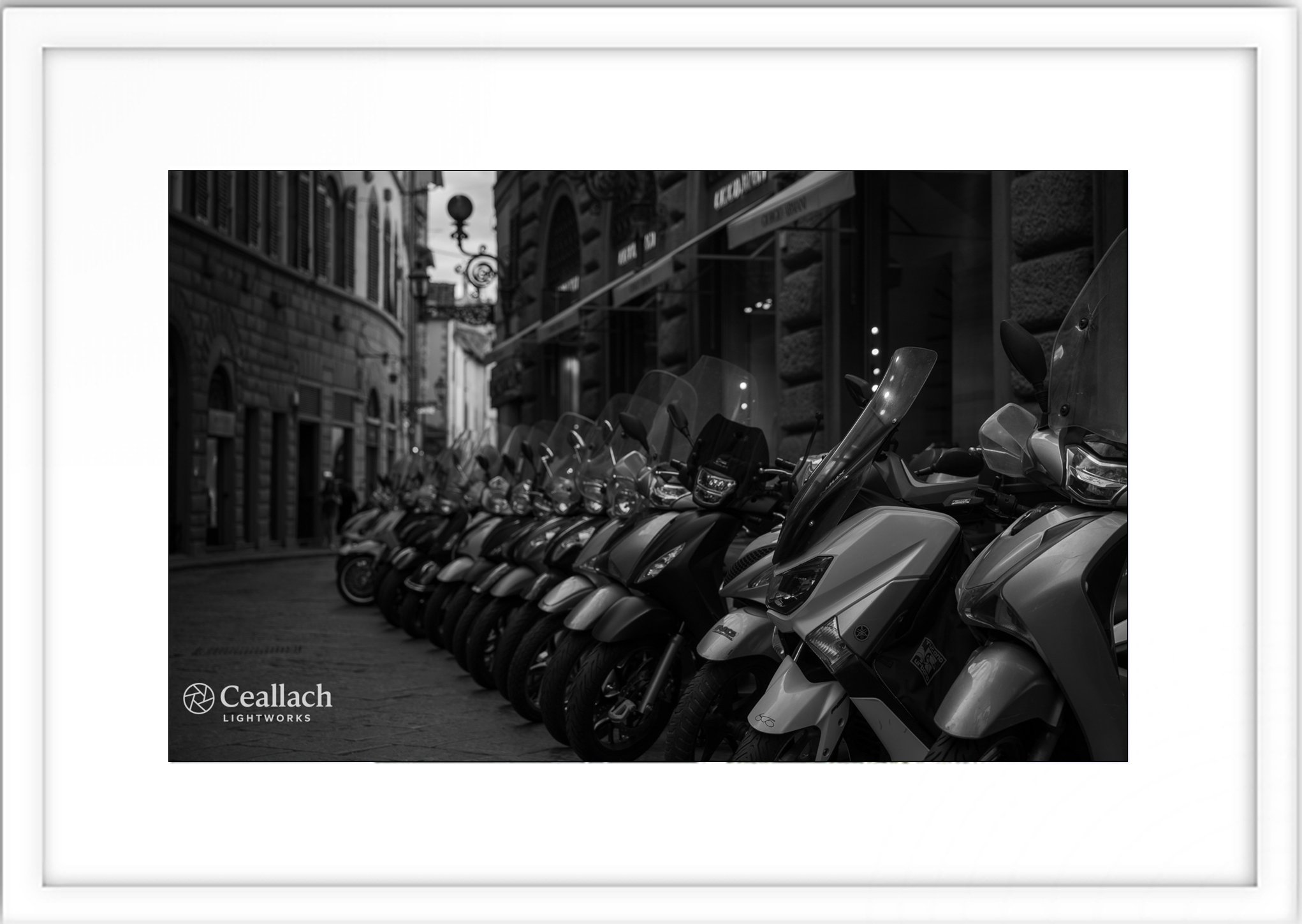 Line of parked scooters on a city street in black and white.