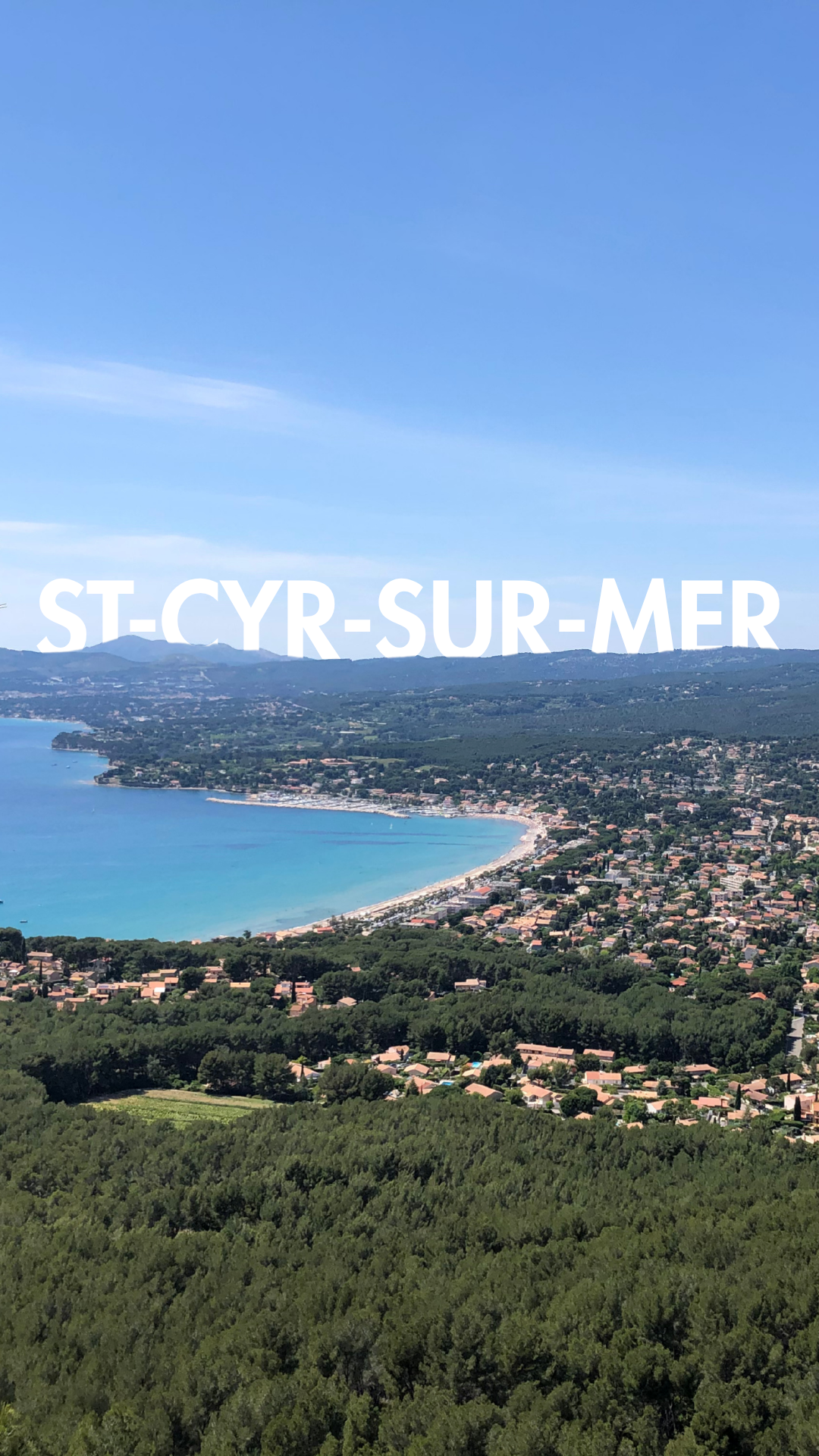 Vue aérienne de la côte de Saint-Cyr-sur-Mer, avec la plage, la mer bleue et des quartiers résidentiels entourés de verdure, sous un ciel bleu.