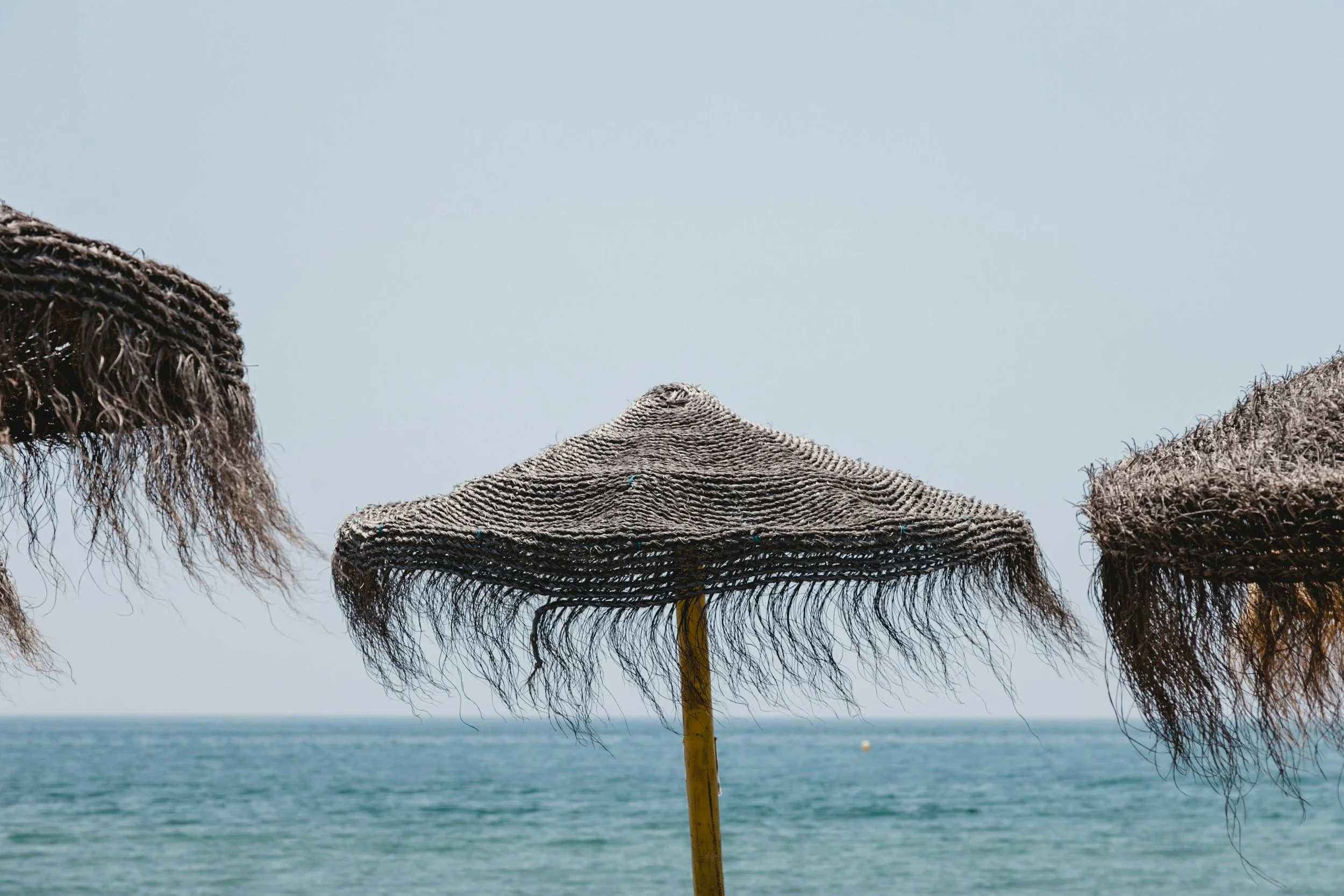 Plage avec trois parasols en paille au bord de la mer