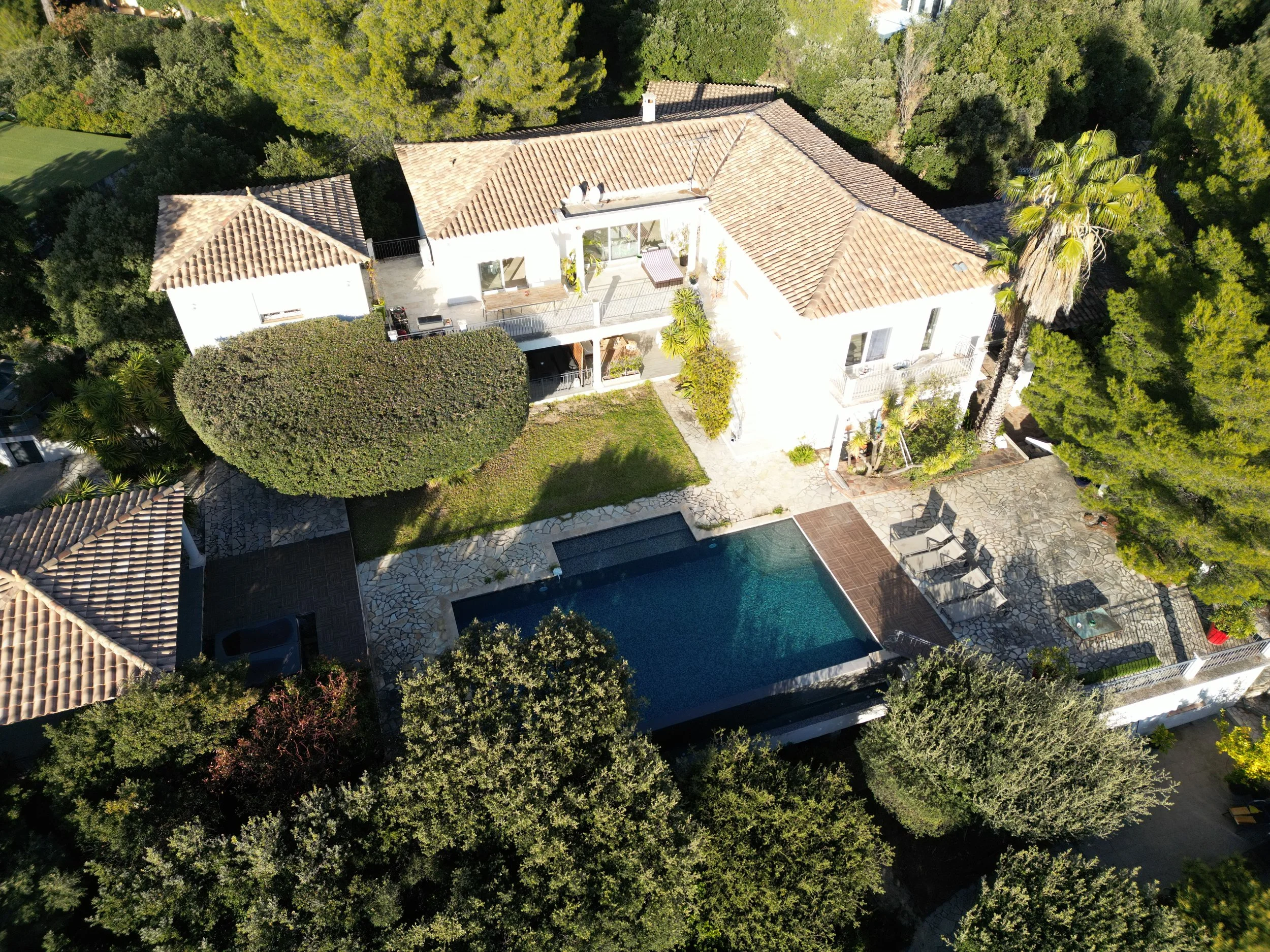 Vue aérienne d'une maison avec piscine, terrasse en pierre, jardin et nombreux arbres environnants.
