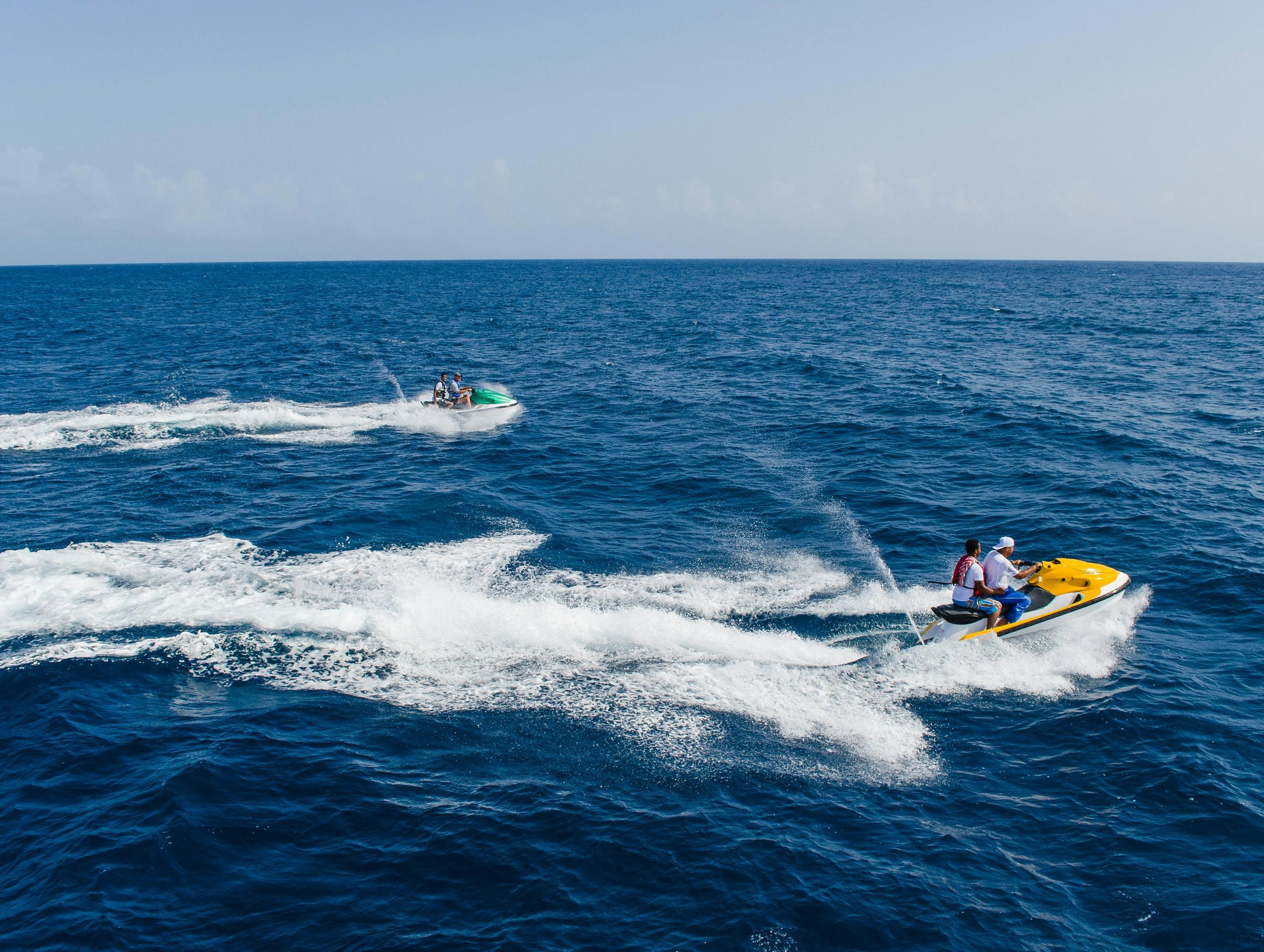 Deux personnes sur une moto marine jaune filant sur l'eau bleue de la mer.