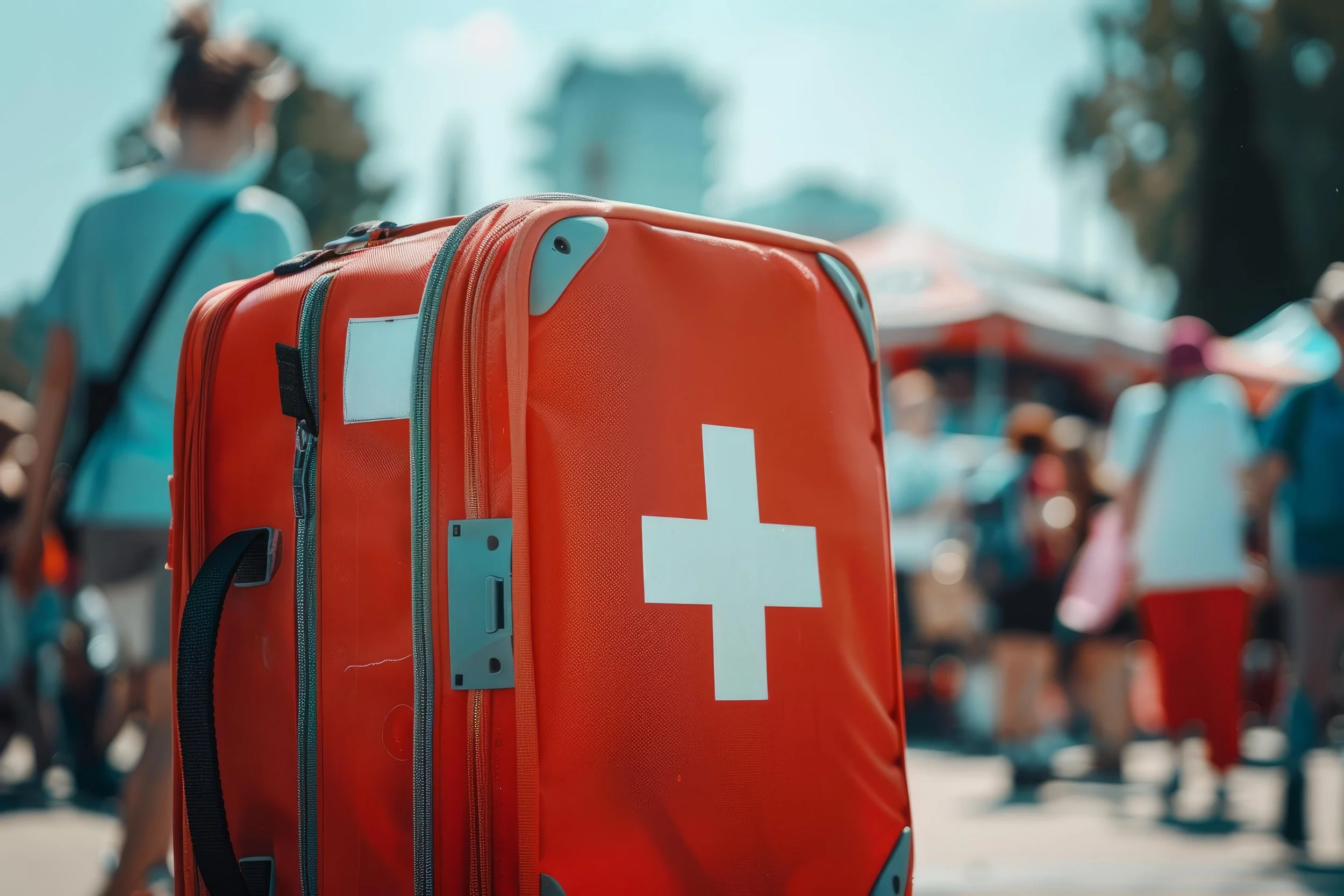 An orange medical emergency or ambulance bag with a white cross symbol on it, in a crowded outdoor setting with blurred people in the background.