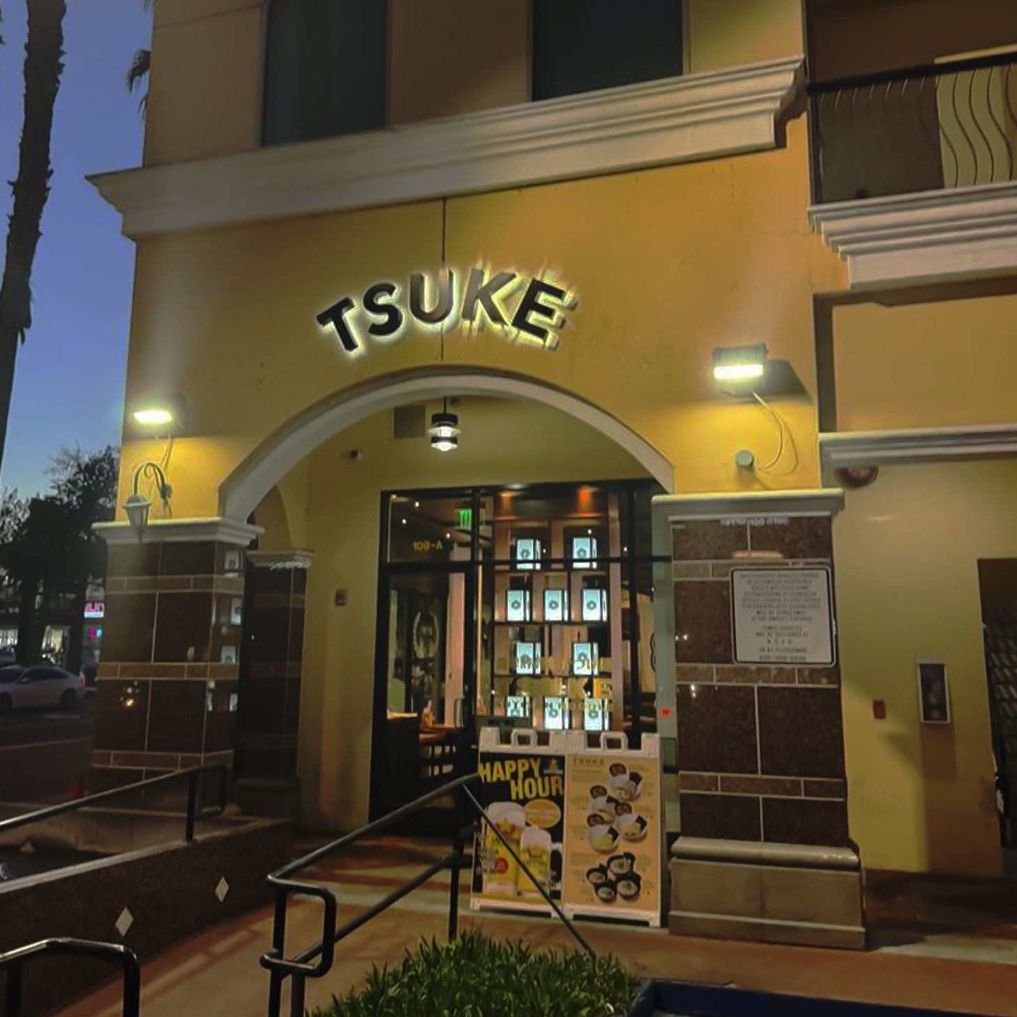 Exterior image of TSUKE store front, with TSUKE text lit up over front entrance