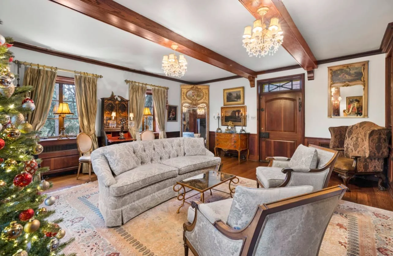 Living room decorated for Christmas with a decorated Christmas tree, elegant sofas, vintage furniture, and artwork on the walls.