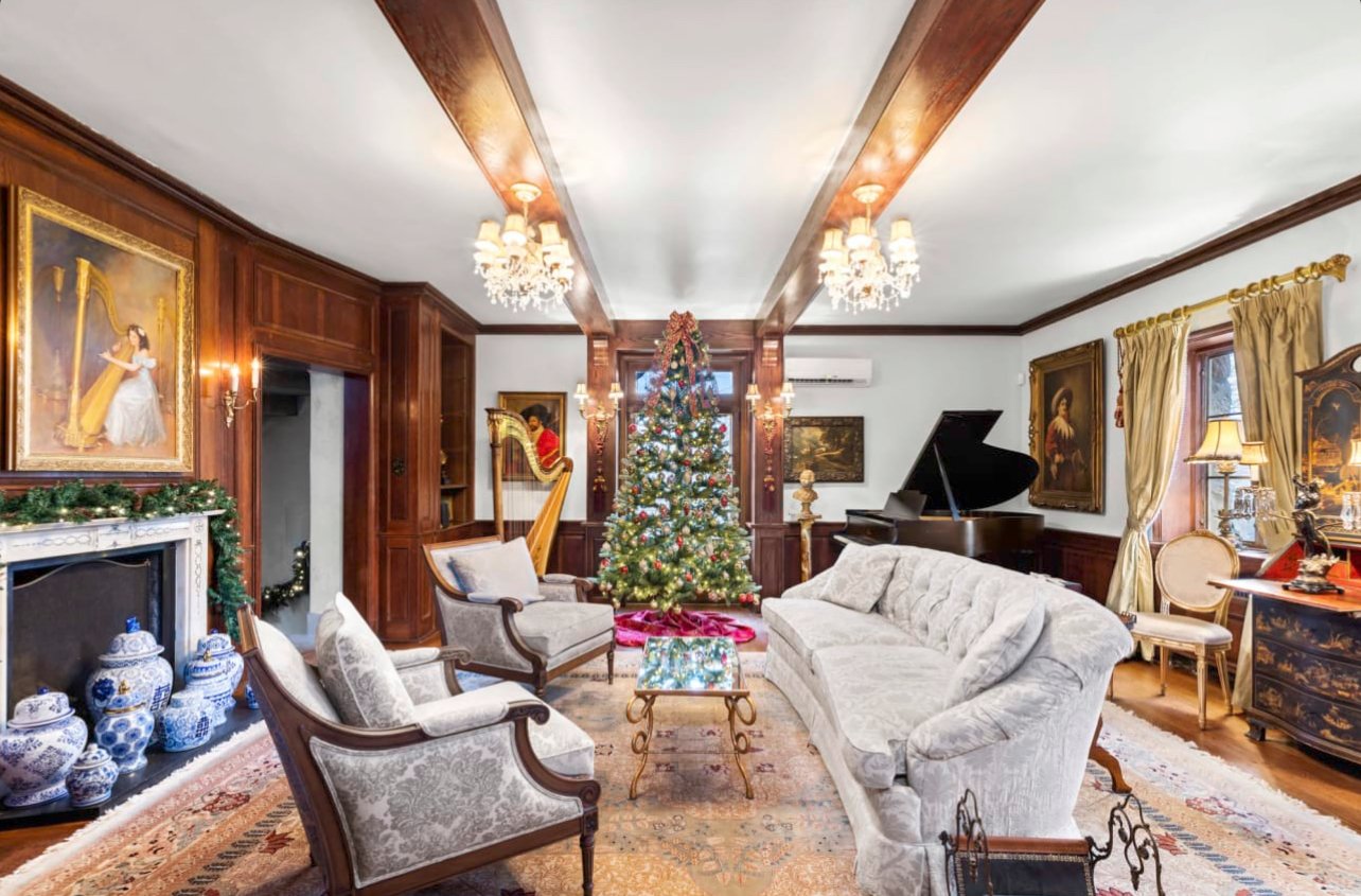 Elegant living room decorated for Christmas with a Christmas tree in the center, surrounded by vintage furniture, a grand piano, paintings, and decorations.