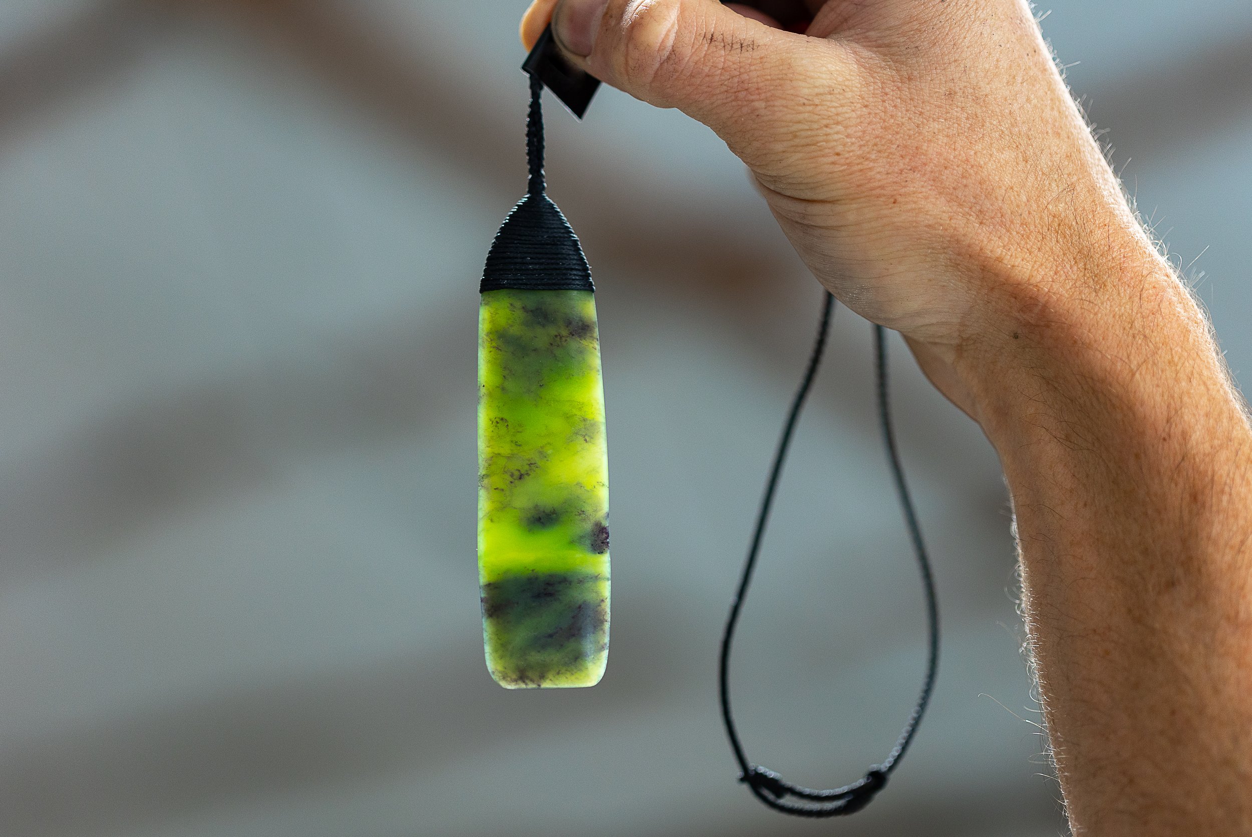 A person's hand holding a green and black marbled pendant necklace.