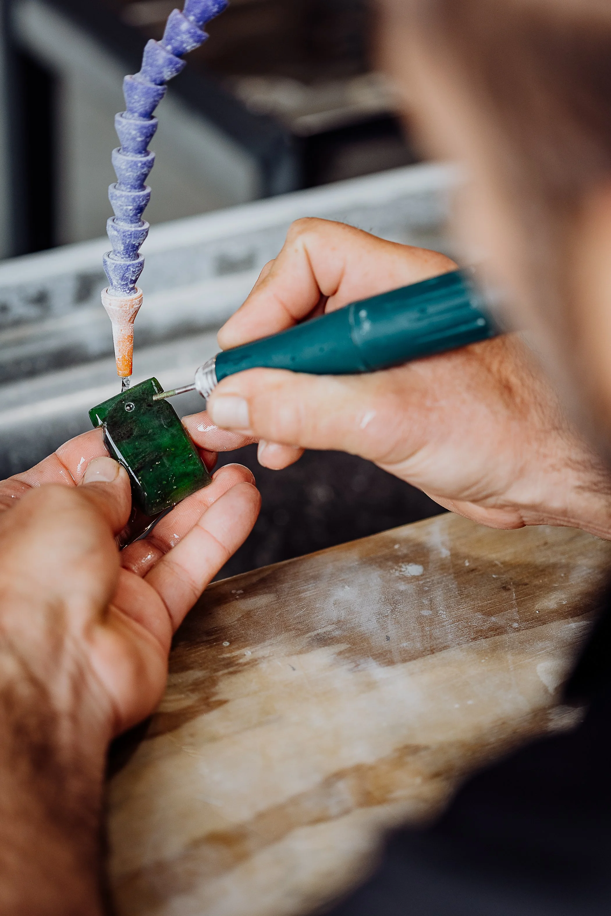 A person working on a small green circuit board with a soldering iron, with a flexible soldering arm in the background.