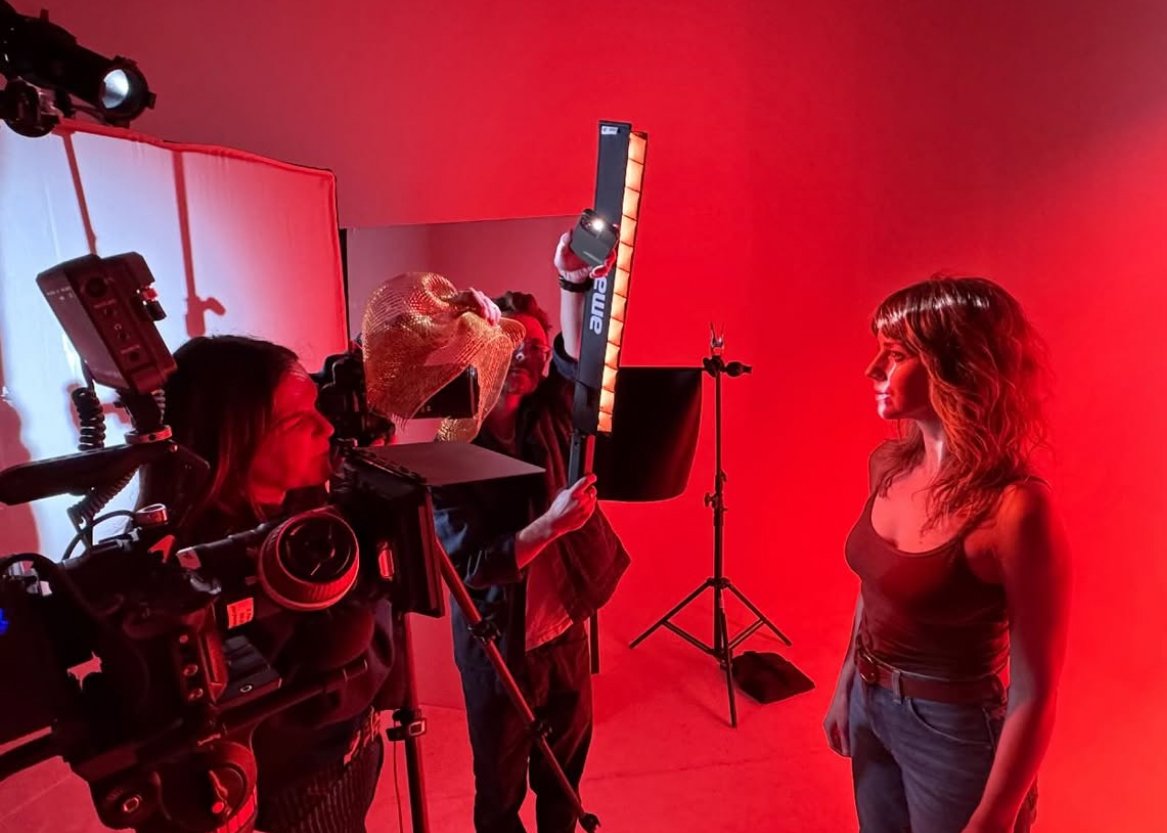 A woman posing for a photo in a studio with red lighting. Cameras and lighting equipment are visible around her.