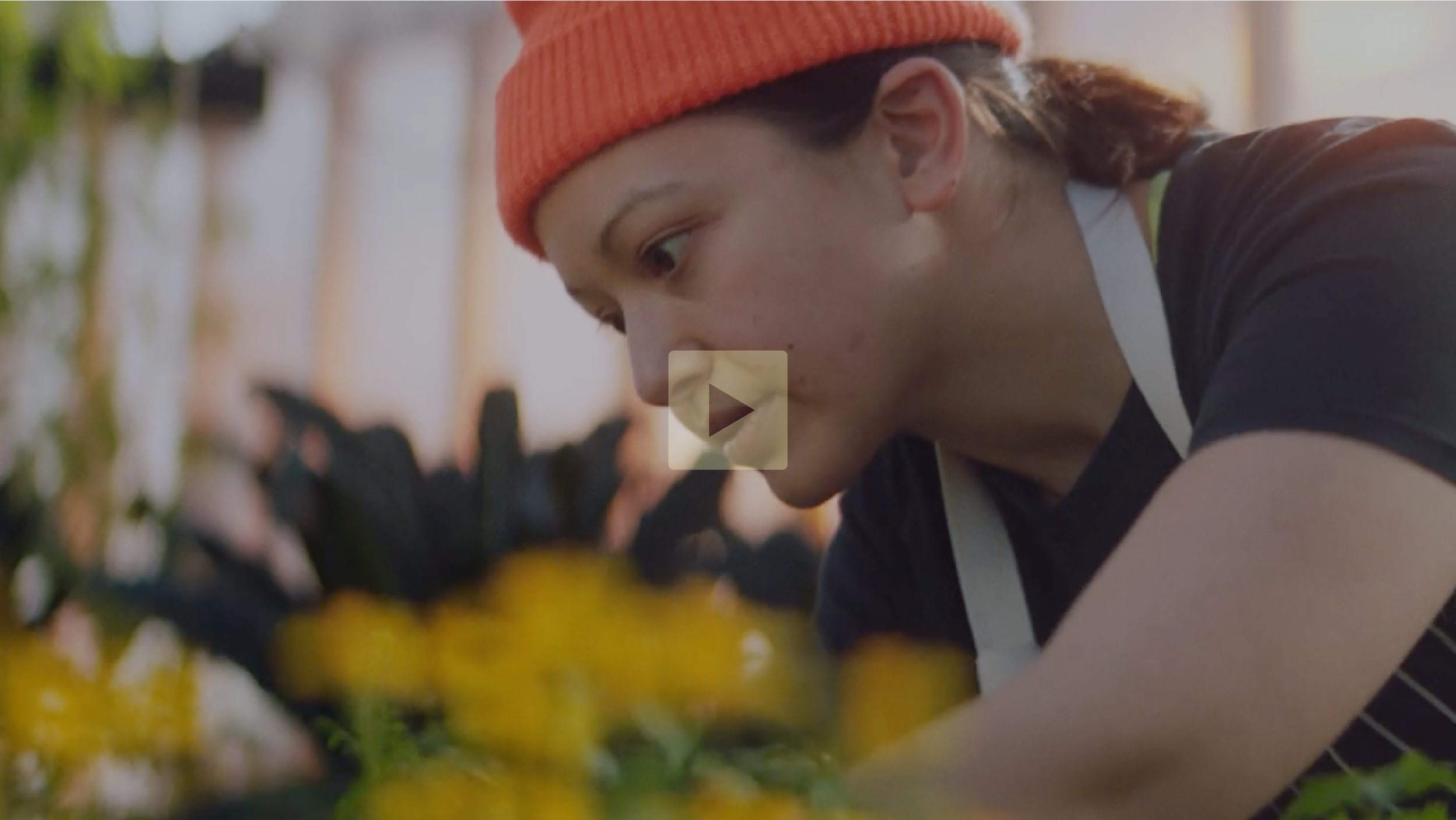 A young person wearing an orange beanie and black t-shirt tending to plants in a garden.