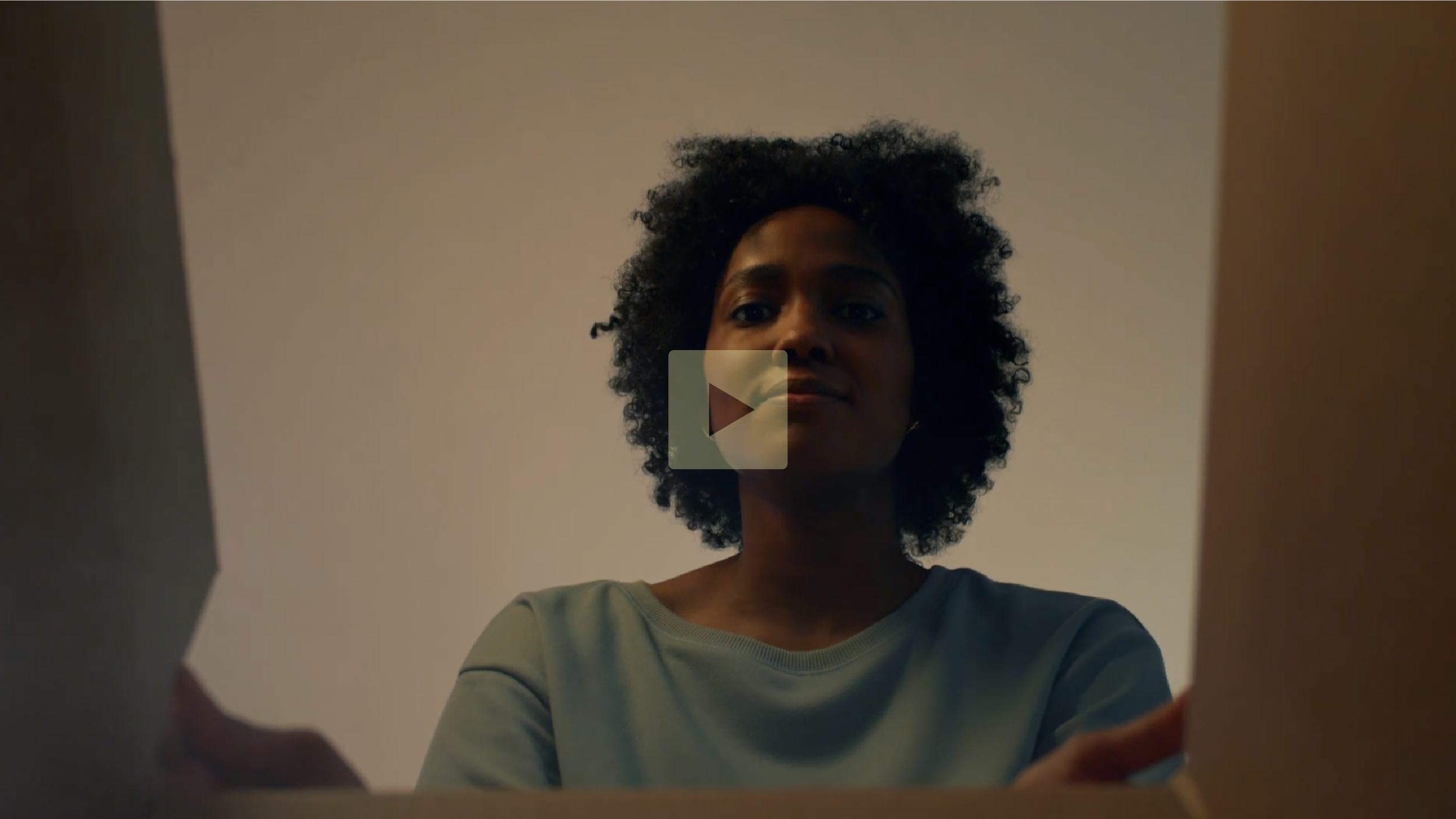 A woman with curly hair looking down at a box, viewed from below with a camera angle from inside the box.