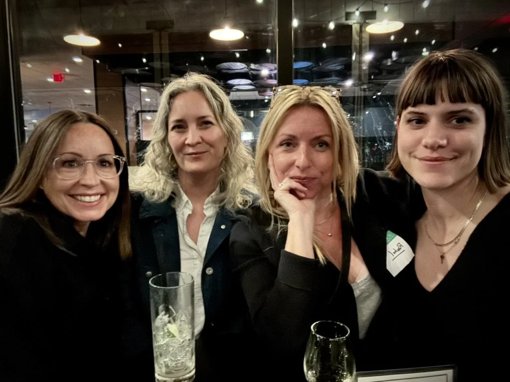 Four women sitting together in a restaurant or bar, smiling for a photo.