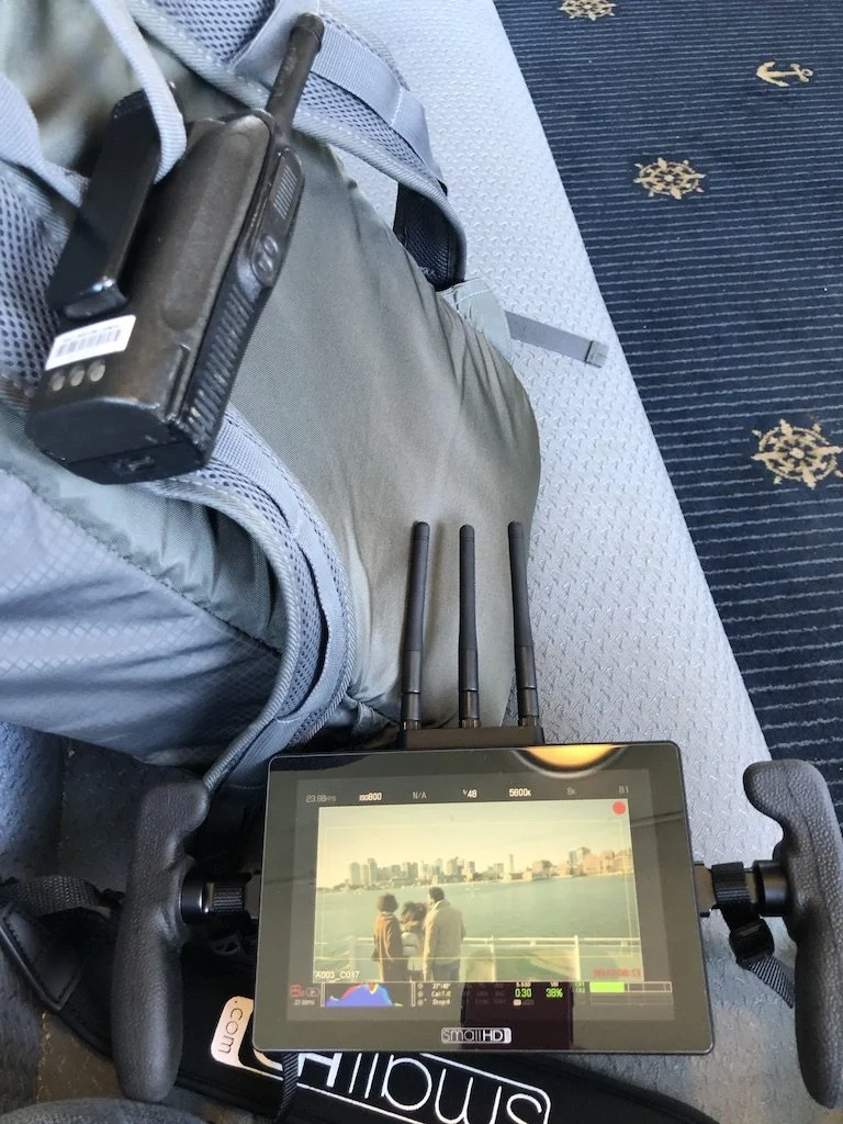 A digital monitor on a wheelchair controls, showing a photo of three people by the water with a city skyline in the background.