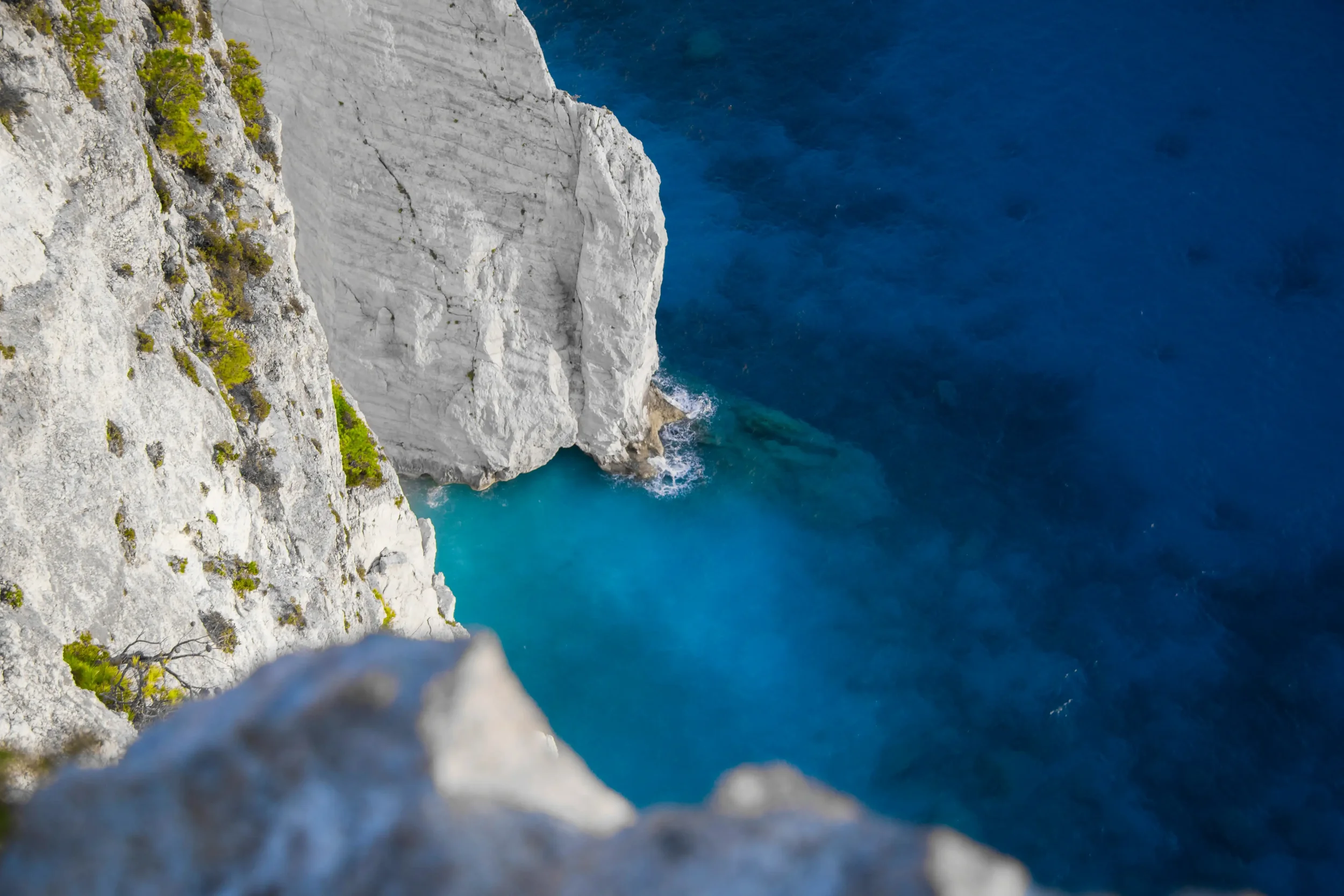 A dramatic high-angle view of steep white limestone cliffs plunging into vibrant, crystal-clear blue ocean water, representing the Off the Radar secluded travel itineraries on Swallow's Notes.