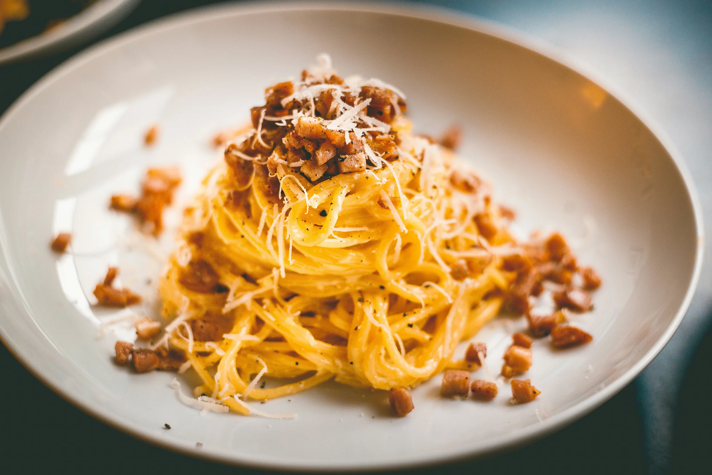 A close-up shot of traditional Roman spaghetti alla carbonara, topped with crispy guanciale and a creamy pecorino and egg sauce.