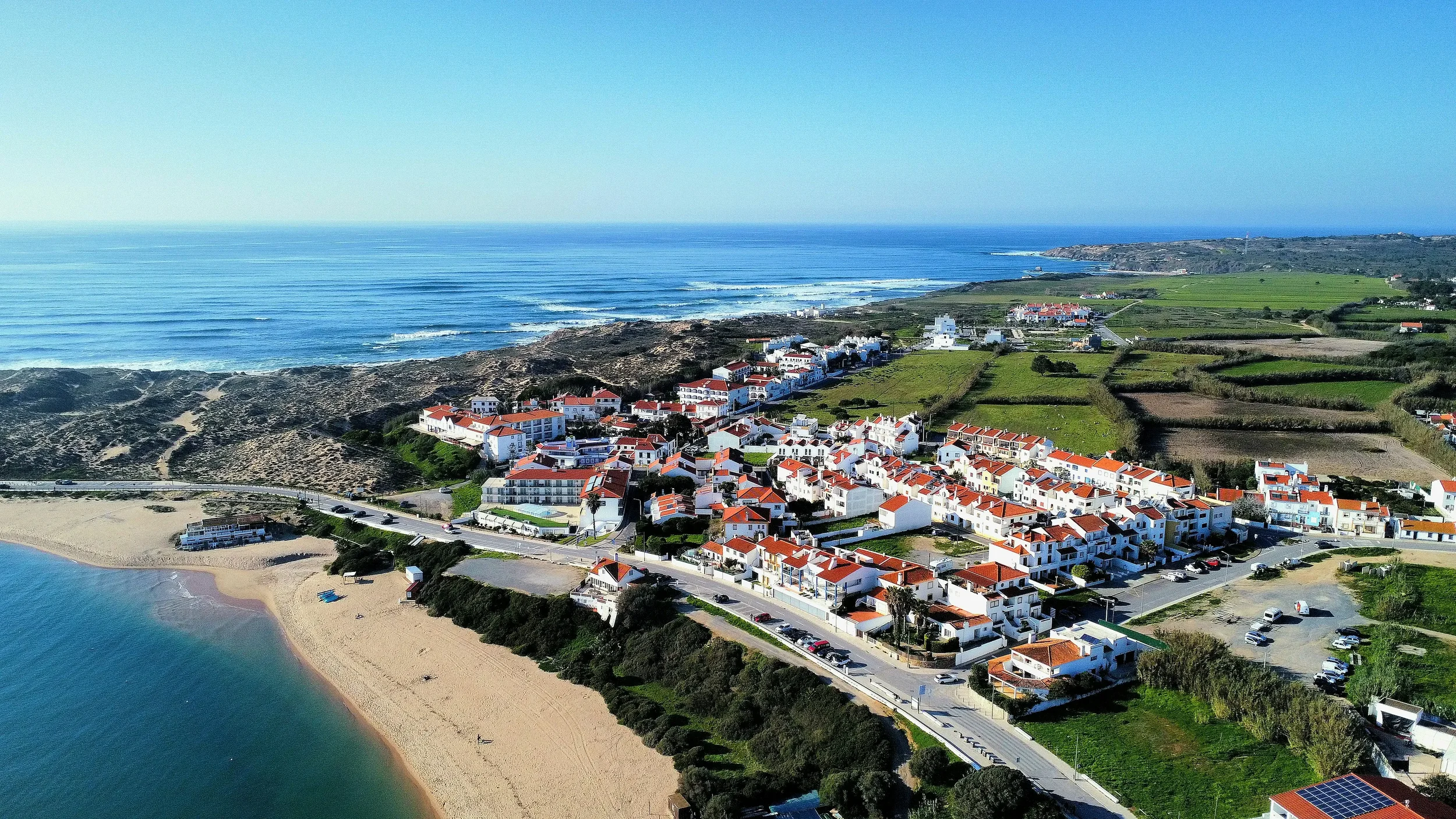 Panoramic view of the white houses of Vila Nova de Milfontes overlooking the calm turquoise waters of the Mira River meeting the Atlantic Ocean in Alentejo.