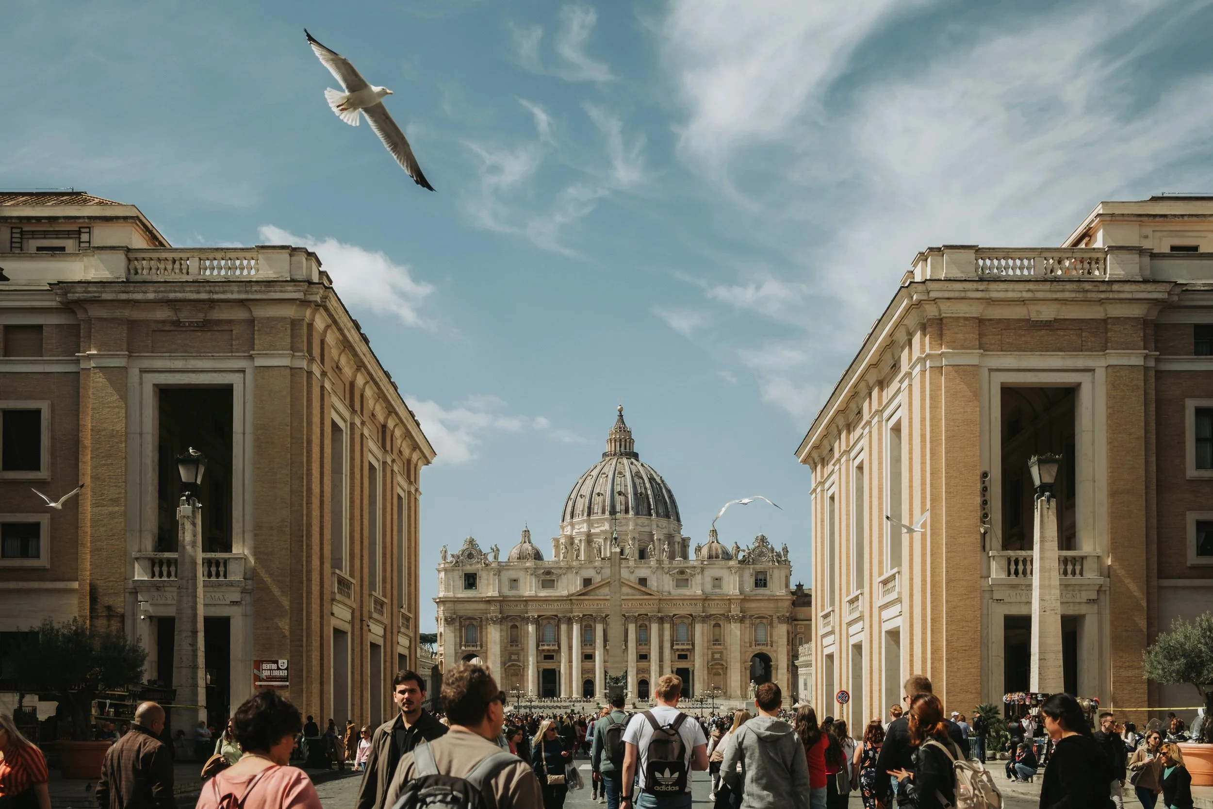 A daytime view of St. Peter's Basilica dome in the distance, framed by the Tiber River and the bridges of Rome.