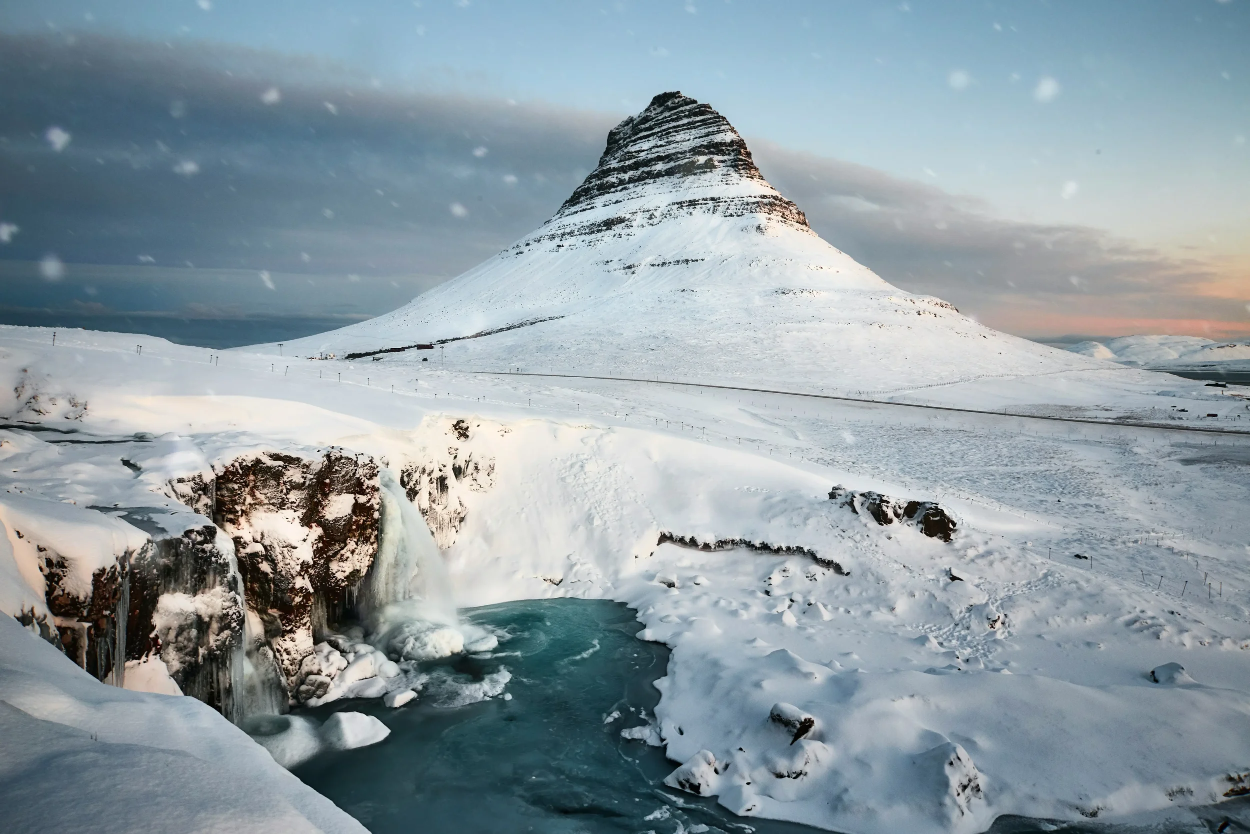 Symmetrical view of the arrowhead-shaped Kirkjufell mountain with the tiered Kirkjufellsfoss waterfall flowing in the foreground under a dramatic Icelandic sky.