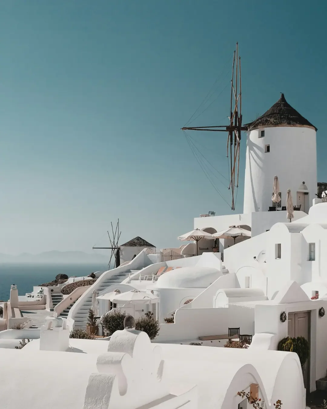 An aerial view of the iconic white-washed houses and narrow streets of Oia, Santorini, overlooking the deep blue Aegean Sea in Greece.