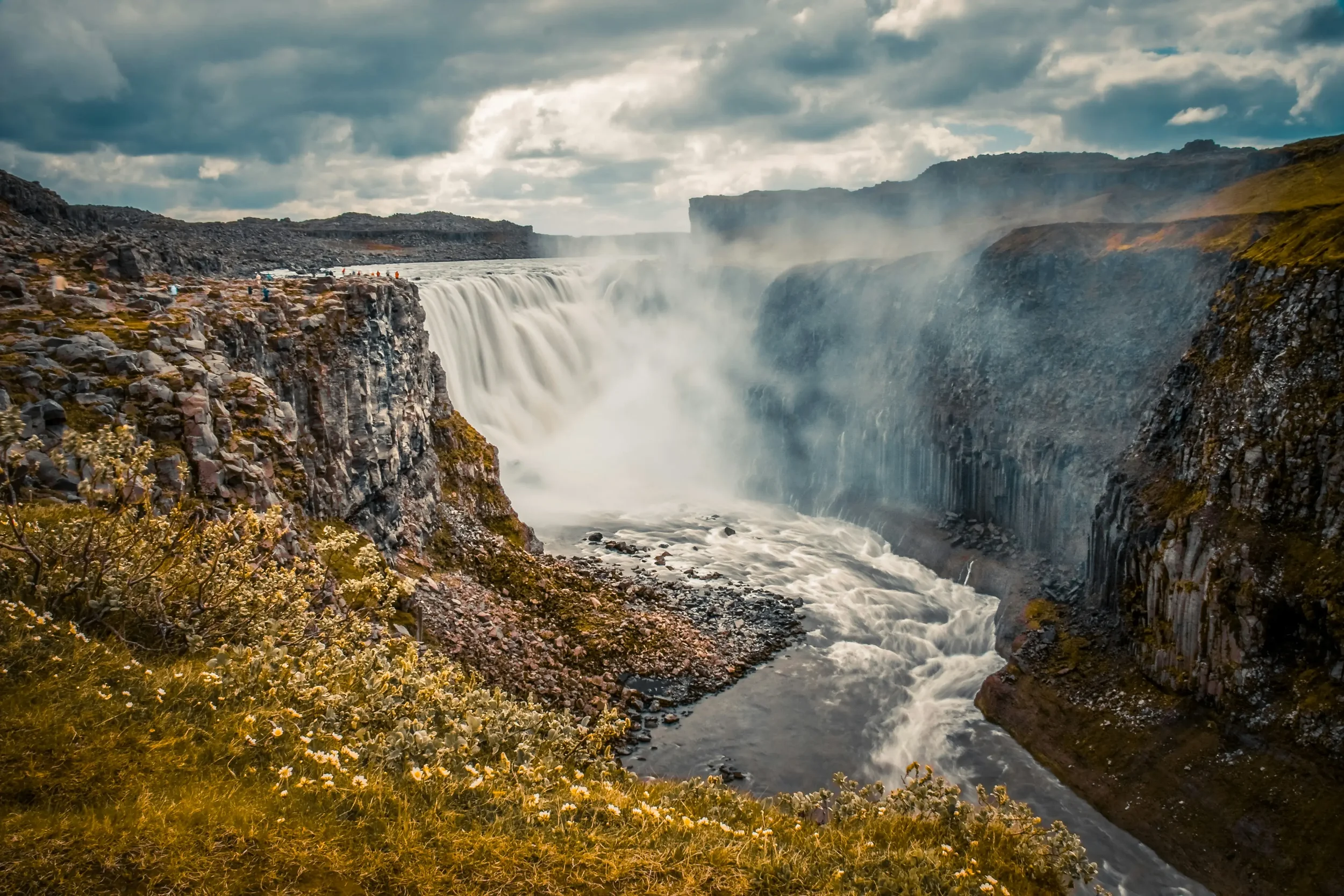 Powerful gray glacial water of Dettifoss waterfall plunging into a deep rocky canyon with rising mist and spray in North Iceland.