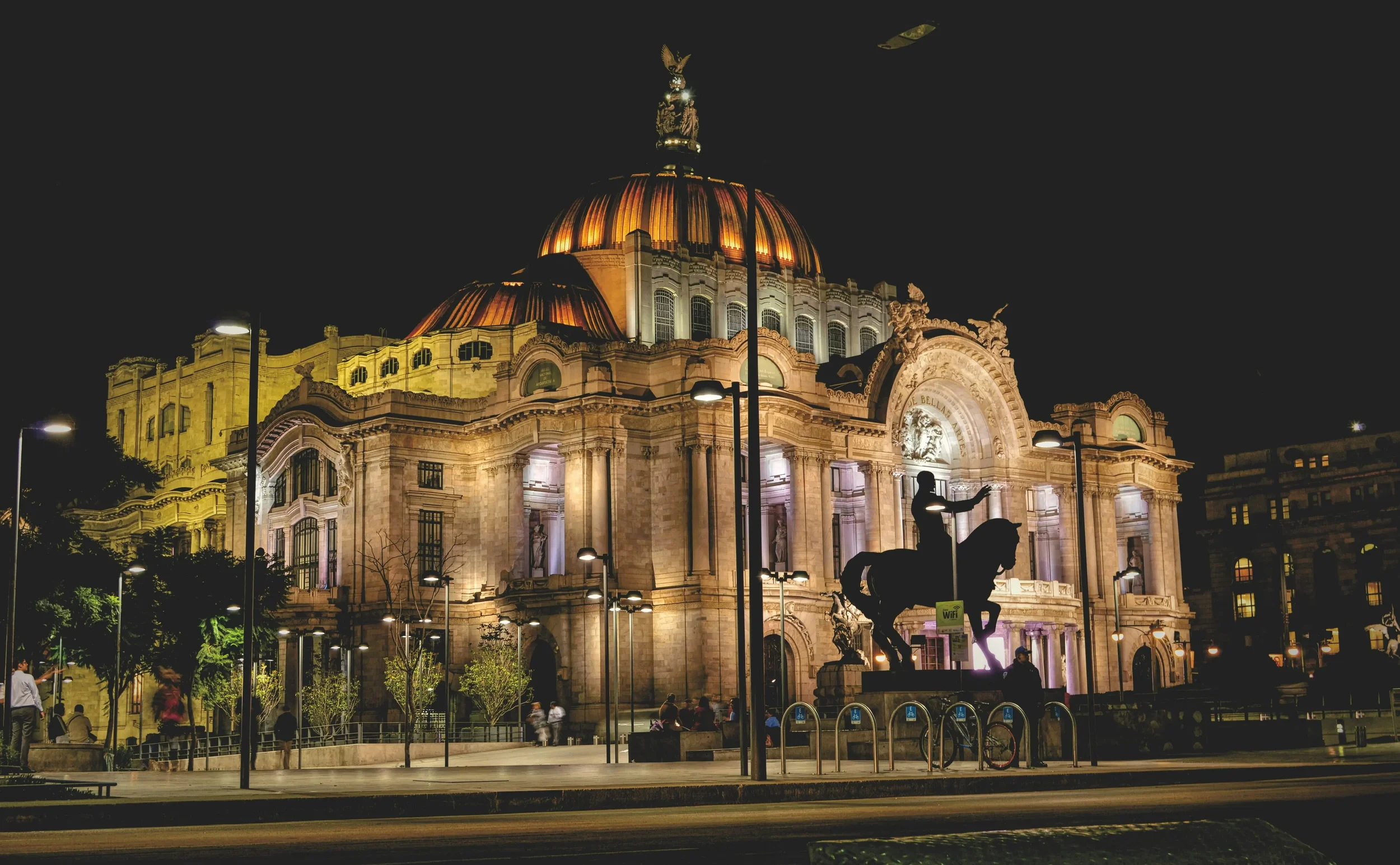 Exterior view of the Palacio de Bellas Artes featuring its iconic orange and yellow tiled dome and Neoclassical architecture in Mexico City.