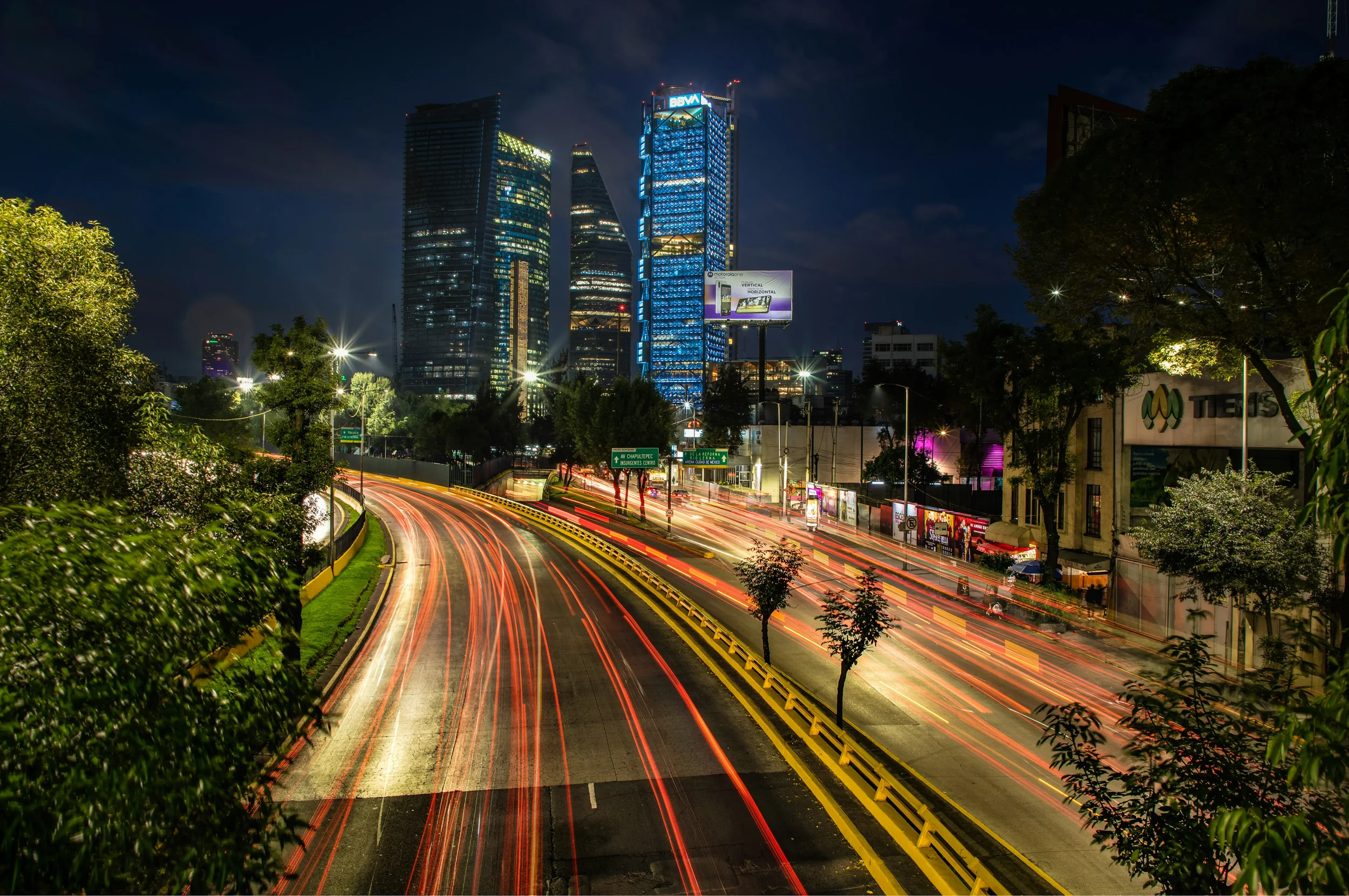 Wide-angle panoramic view of the Mexico City skyline at night with illuminated skyscrapers and city lights under a dark blue sky.