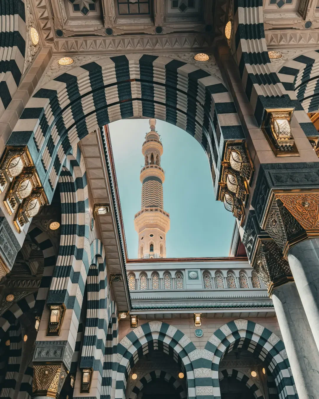 A wide view of Al-Masjid an-Nabawi (The Prophet's Mosque) in Medina, Saudi Arabia, featuring its iconic large convertible umbrellas and tall minarets.