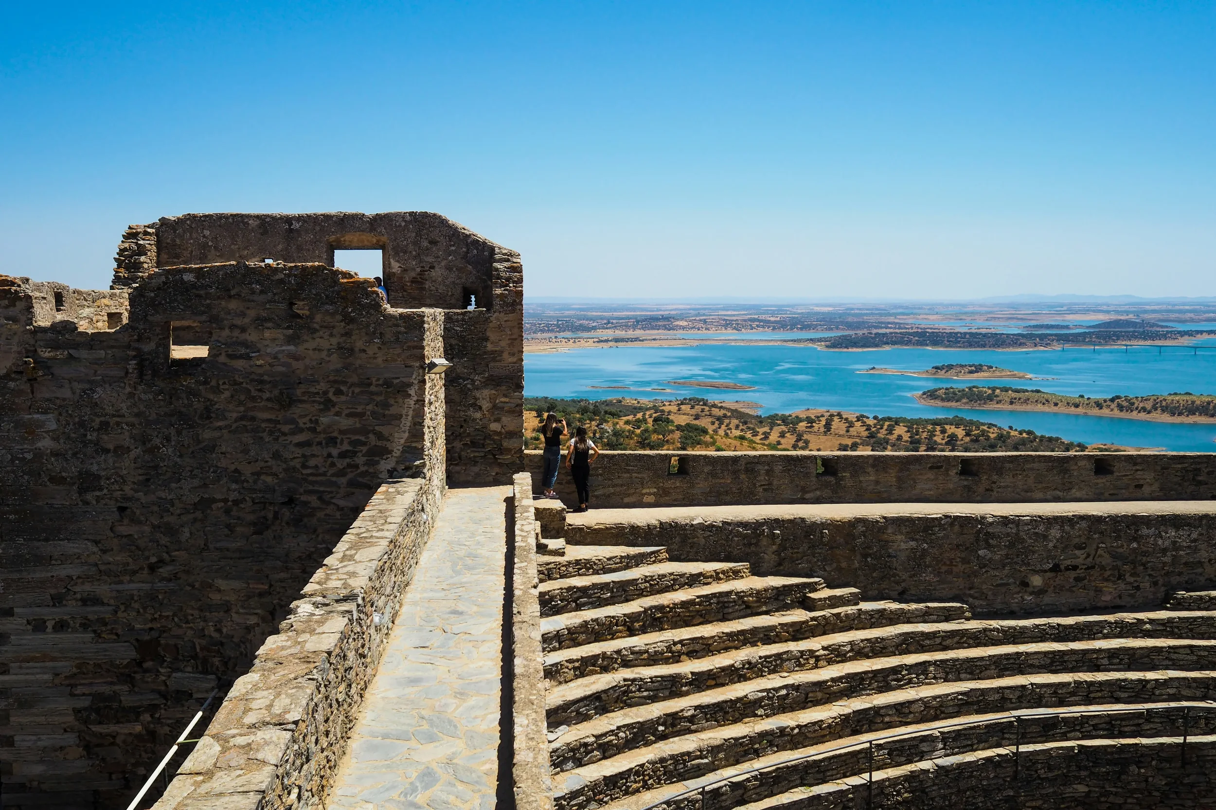 Scenic view of the white-washed houses and narrow cobblestone streets of the medieval village of Monsaraz in Alentejo, Portugal, with the Alqueva lake in the background.