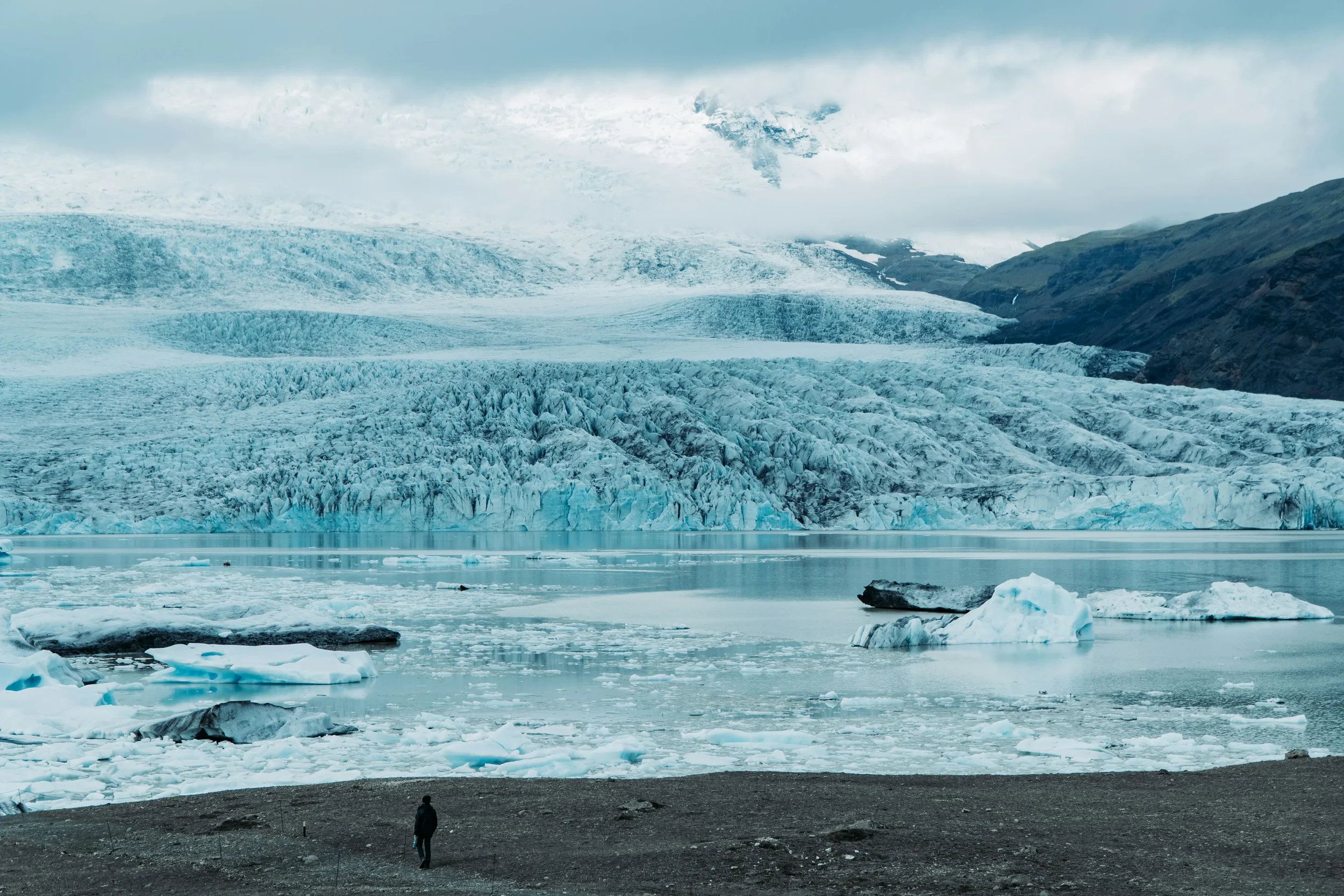 Large blue and white icebergs floating in the calm waters of Jökulsárlón glacier lagoon with the Vatnajökull ice cap in the background under a soft arctic light.