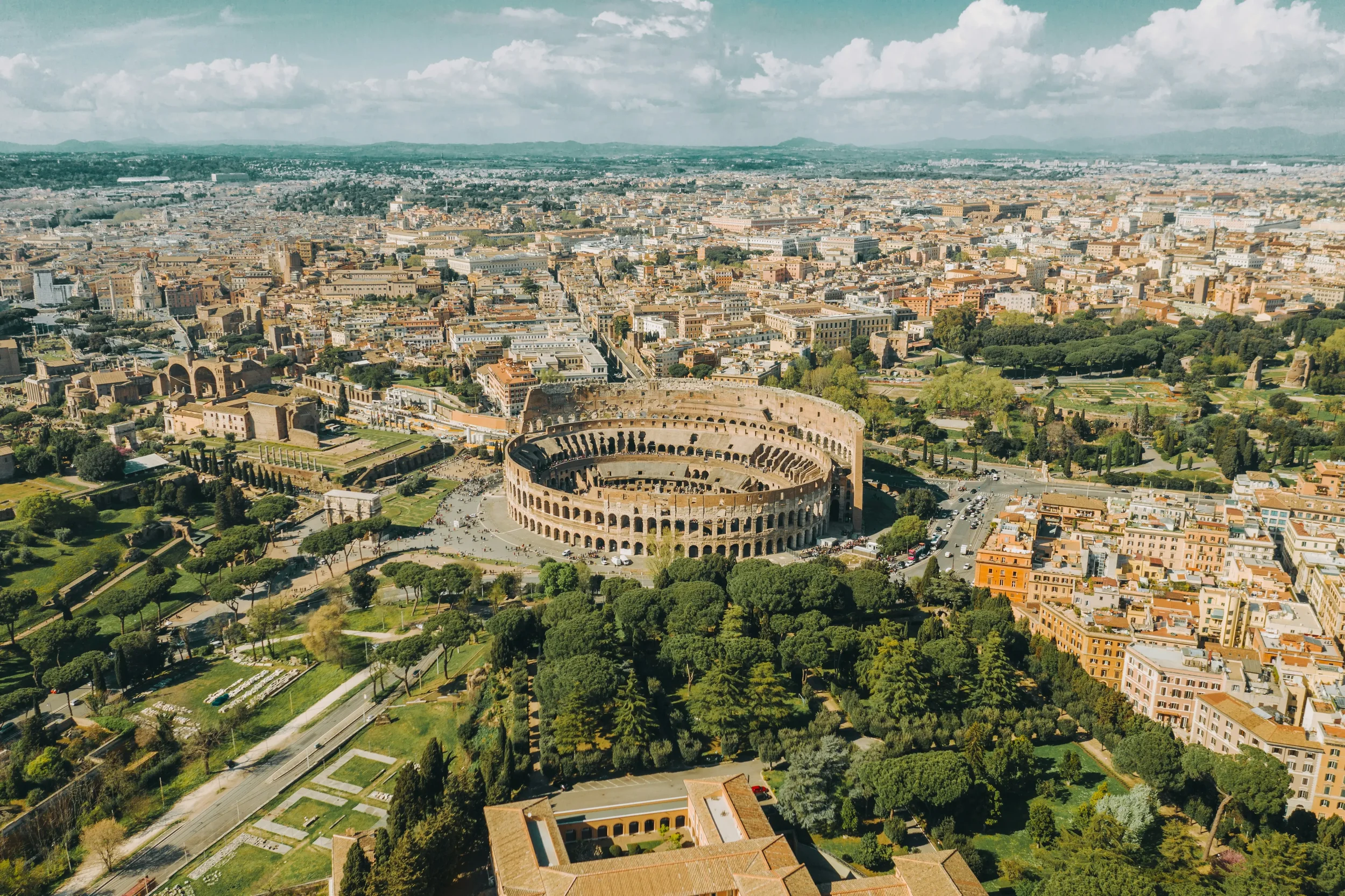 An expansive aerial view of the Roman Colosseum and the surrounding ancient ruins and modern cityscape of Rome, Italy.