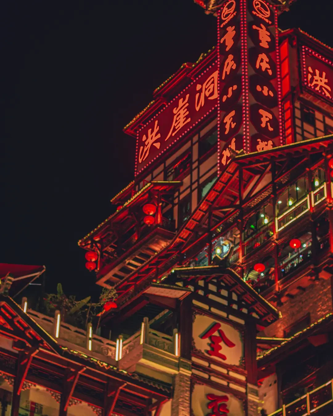 A brightly lit multi-story Chinese building at night with red neon signs and red lanterns, featuring traditional architectural elements and Chinese characters.