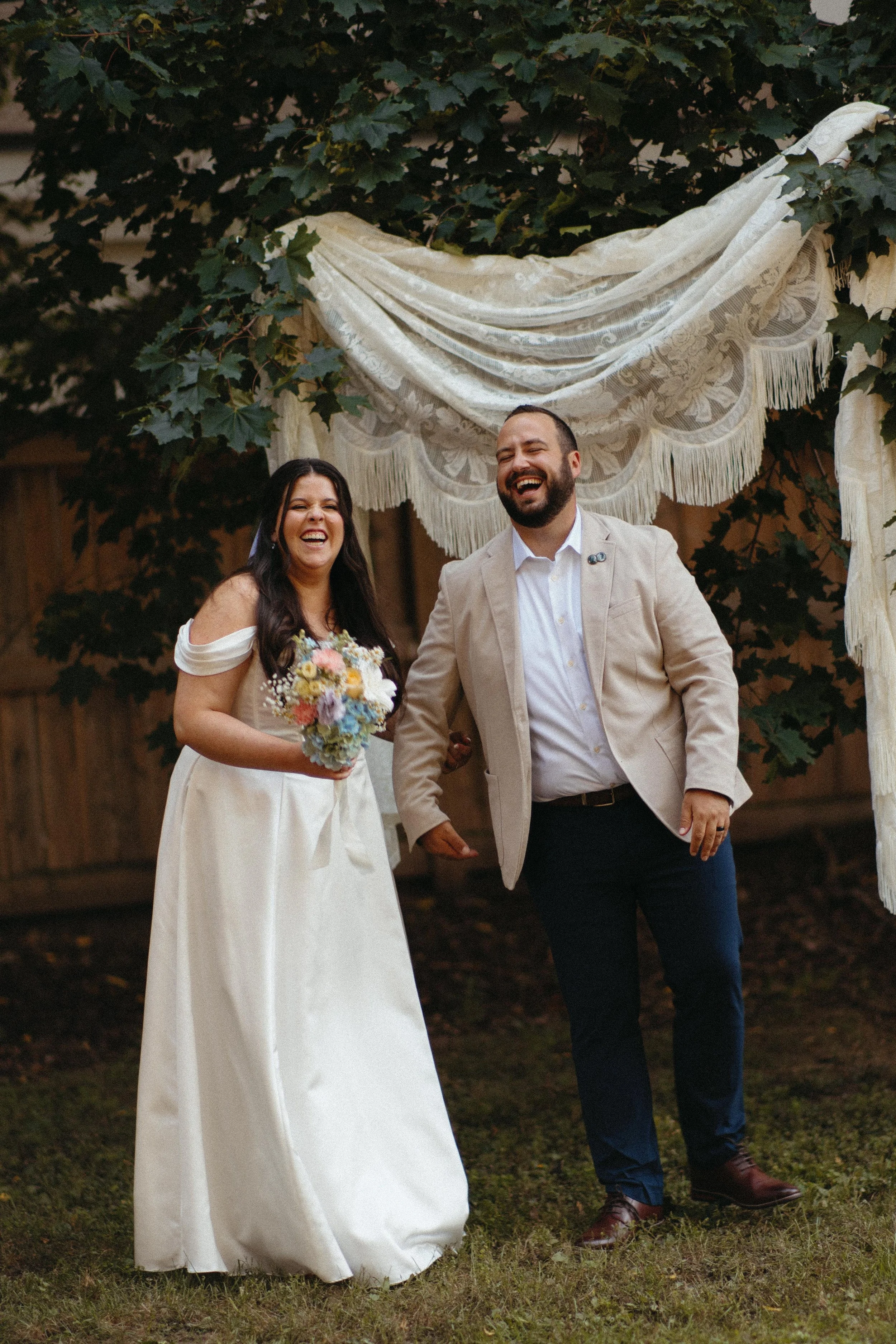 Modern wooden house or cabin on a grassy hillside with trees, overlooking a lake and mountain range in the distance, during sunrise or sunset.
