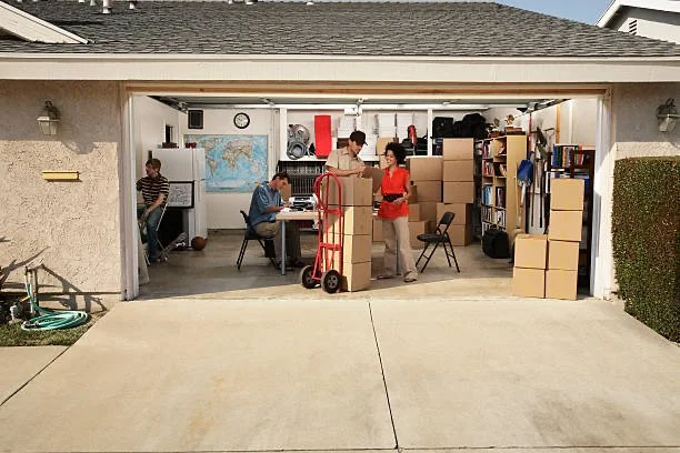 People moving and organizing boxes inside a garage with various household items and furniture.