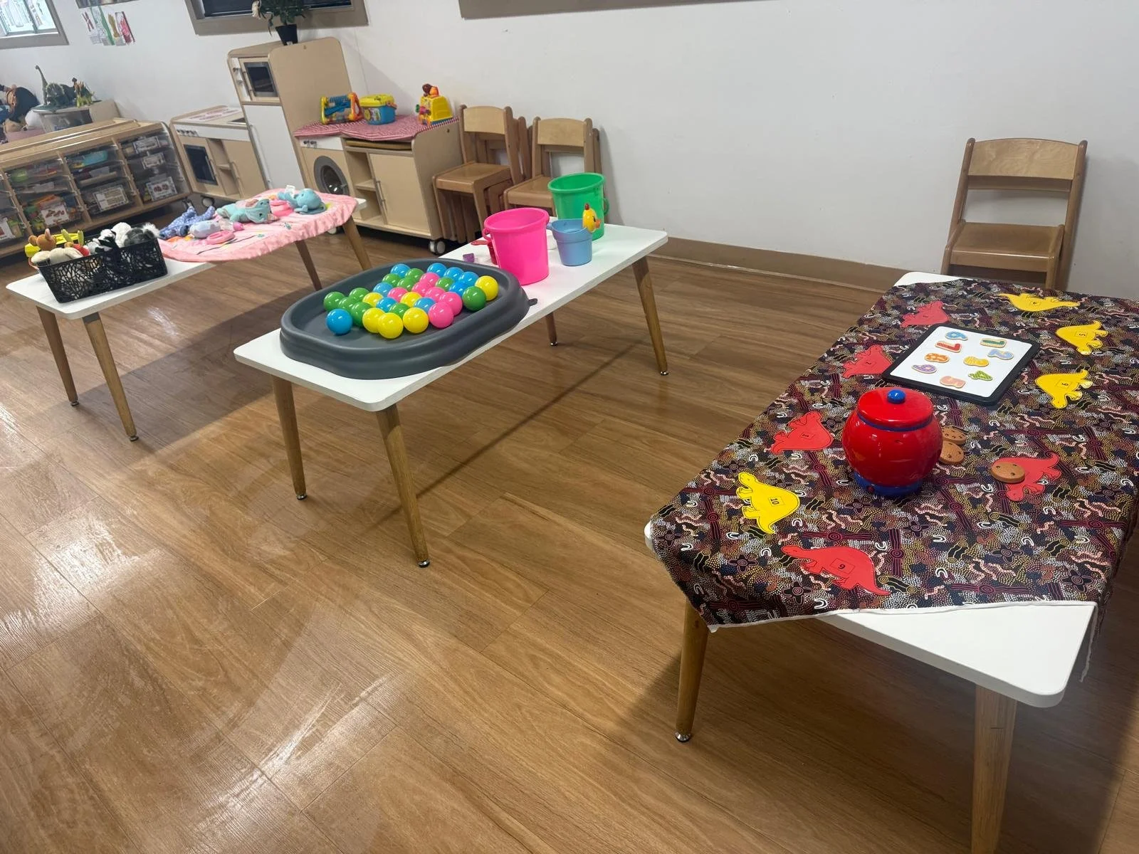 Children's play area with tables and toys, including plastic eggs, buckets, animal puzzles, and play kitchen items.