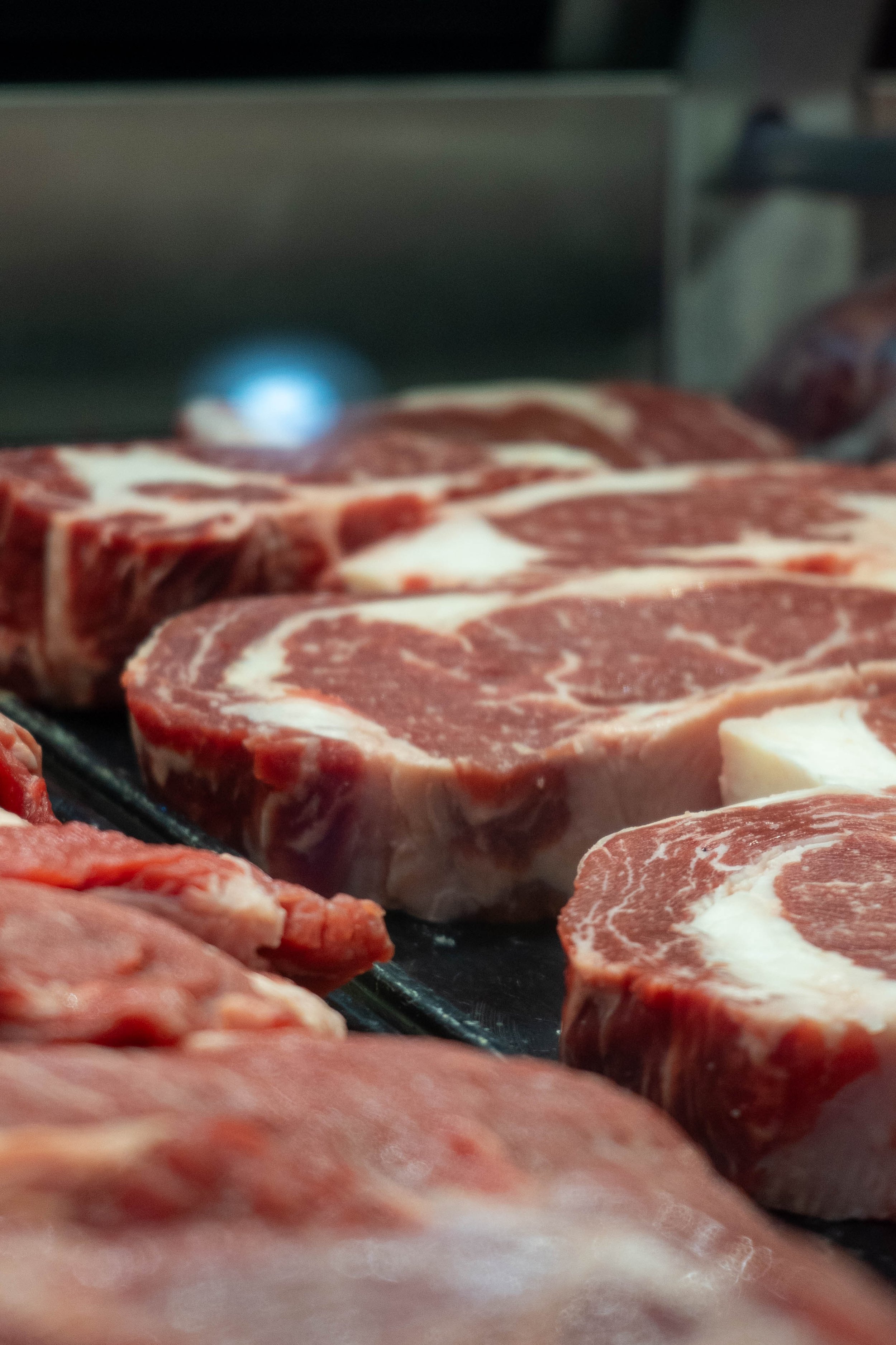 Several raw ribeye steaks on a black tray in a meat store display.
