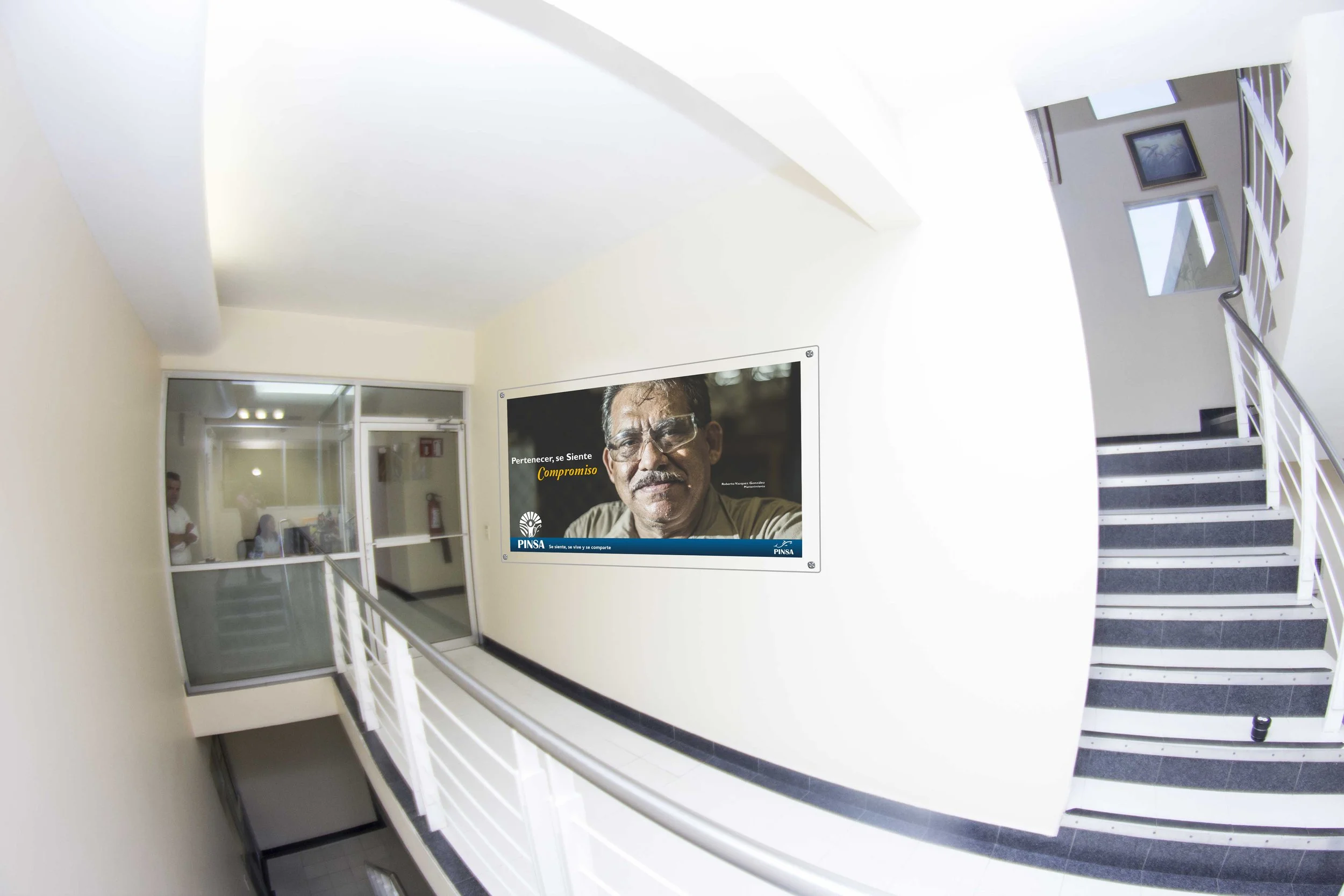 Interior view of a building's corridor with a staircase on the right, white walls, and a large advertisement with a man's face on the wall.