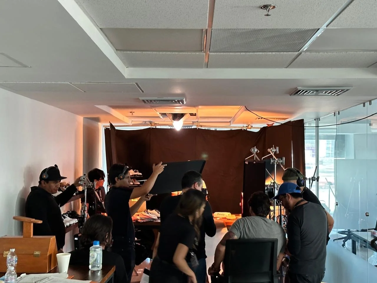 Filmmaking crew setting up a scene in a studio with a dark backdrop, various lighting and camera equipment, and crew members preparing for filming.