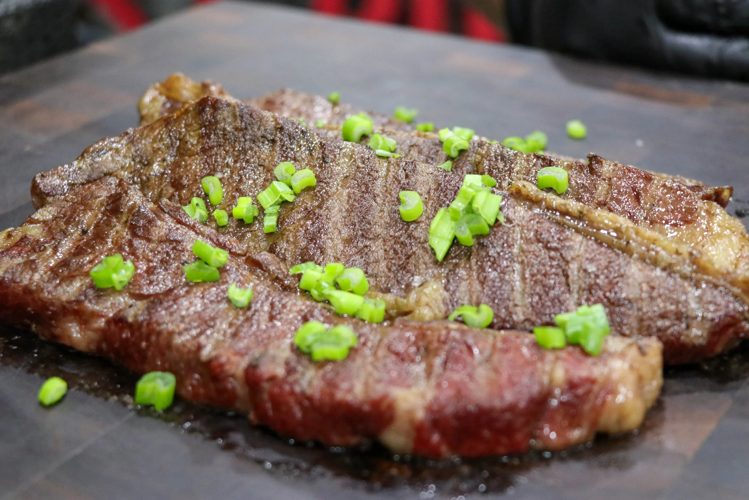 Grilled steak topped with chopped green onions on a dark cutting board.