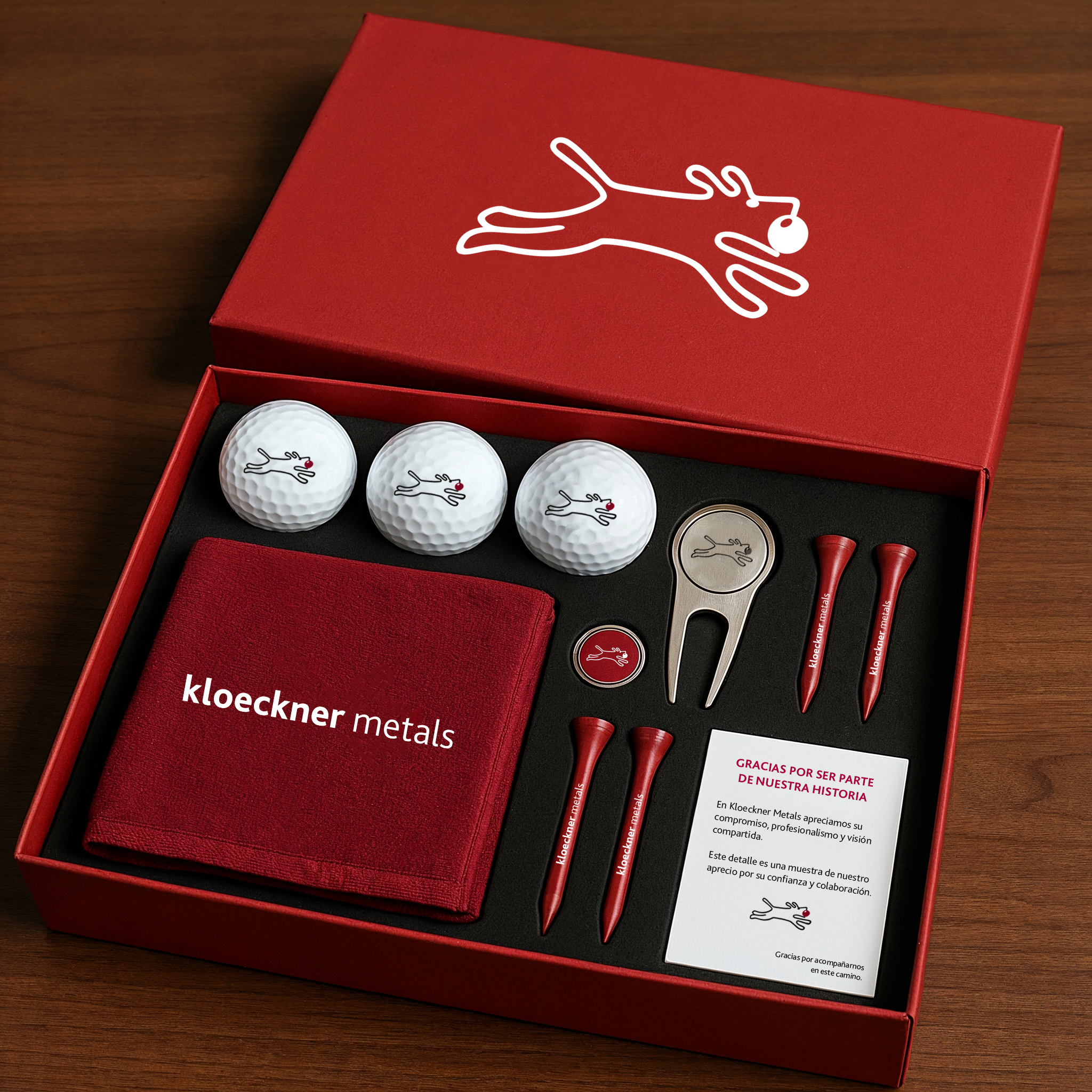 A red gift box with golf-themed items inside, including three golf balls with a logo of a running dog with a red tongue, a golf tee set, a golf divot tool, a red cloth with 'kloeckner metals' written on it, and a note of appreciation.