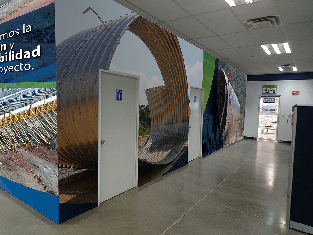 Interior of an office with a large wall mural depicting industrial construction, including a large metal pipe, construction equipment, and a construction site background.