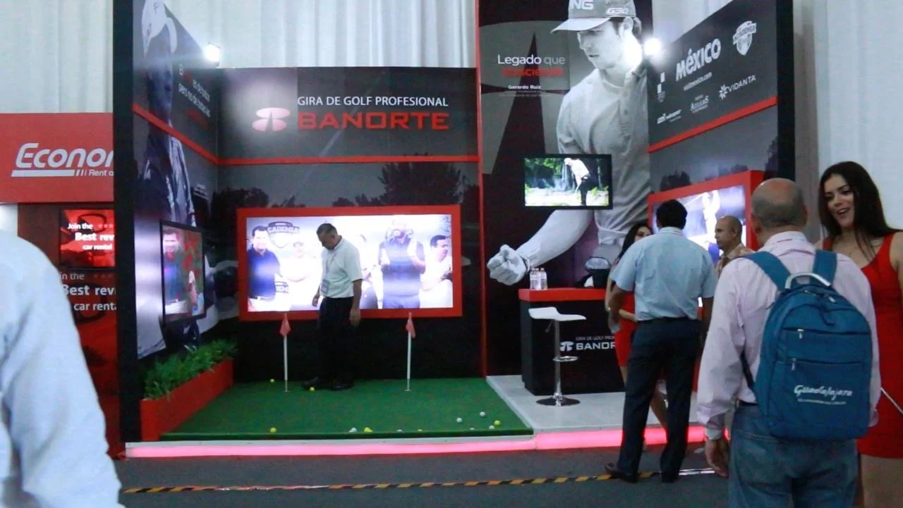 Booth displaying golf simulator and promotional materials for Gira de Golf Profesional Bandorte at an indoor event.