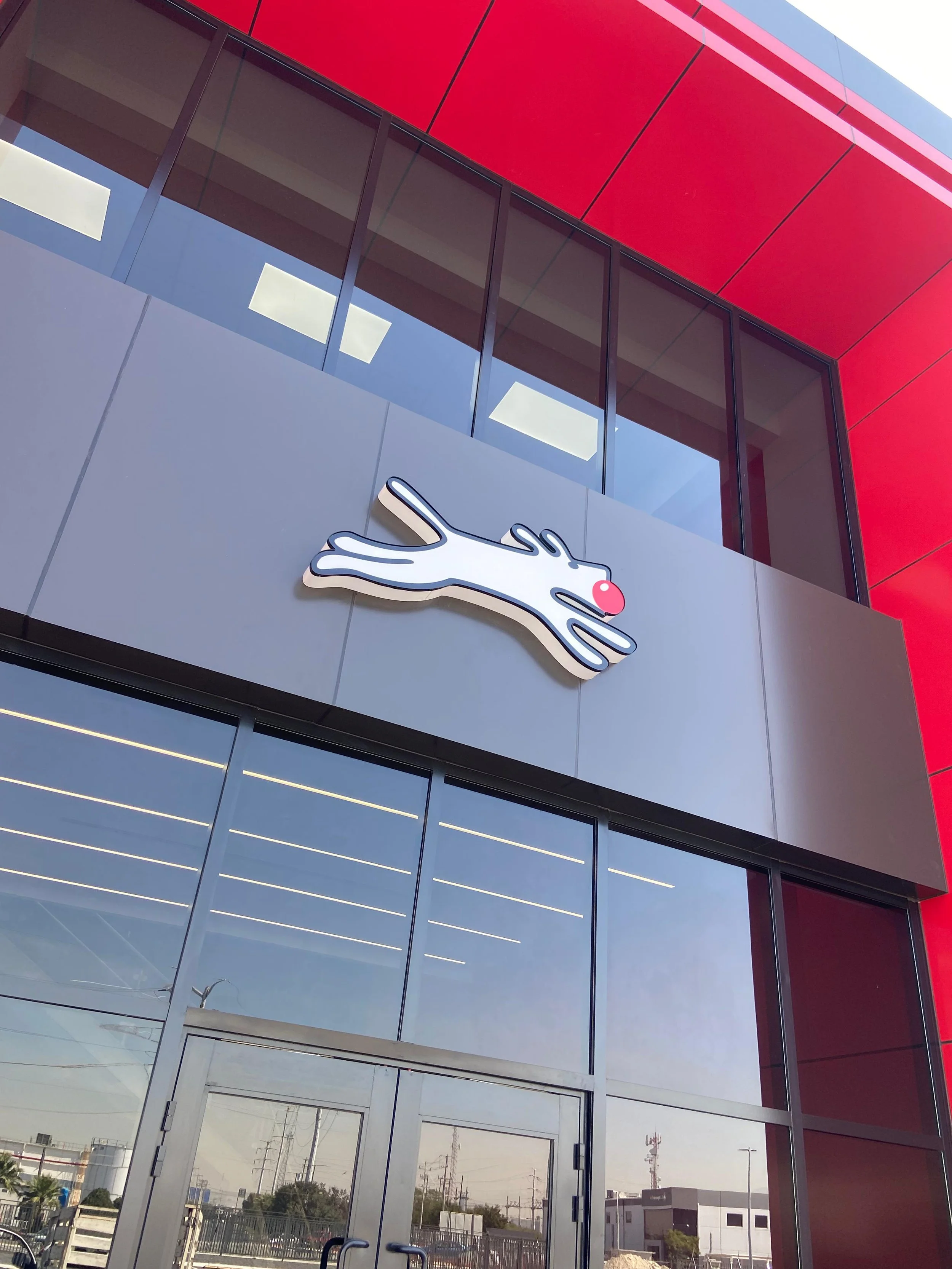 Exterior of a building with a large sign of the Meow Wolf entertainment company, featuring a stylized, cartoon-like white cat with a pink nose, on a gray panel above the entrance.