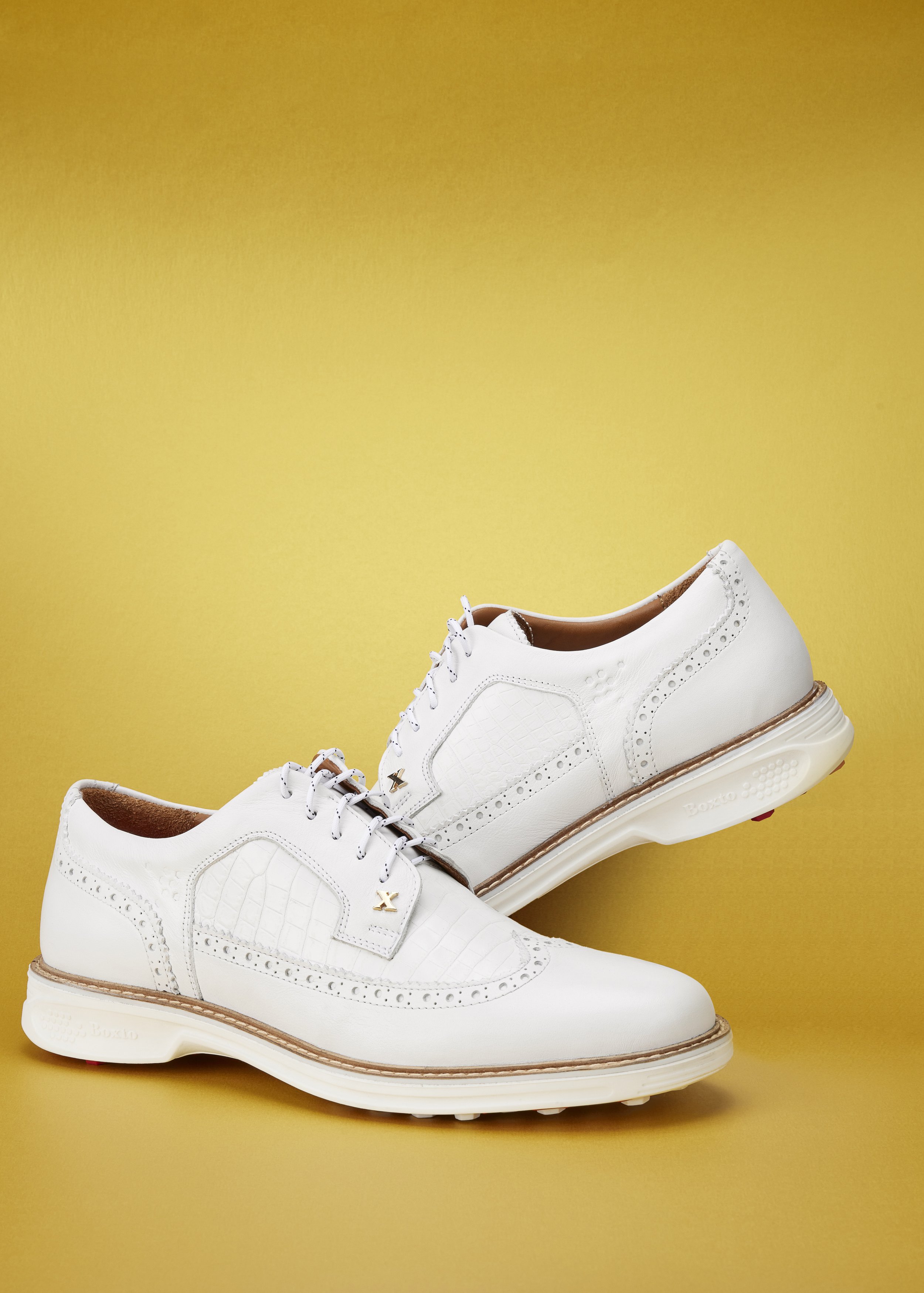 Pair of white men's dress shoes with brogue detailing and a textured pattern on a yellow background.