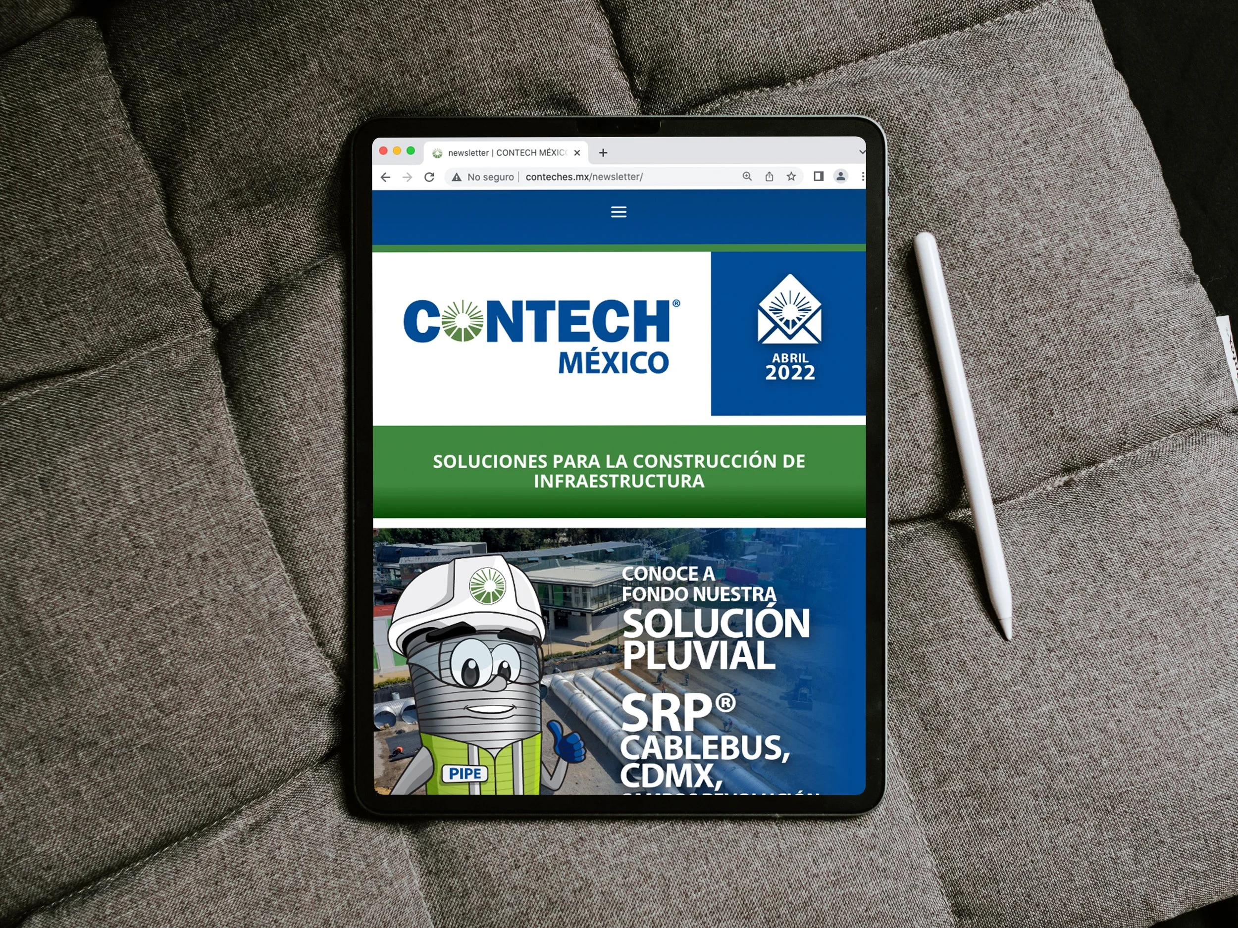 Tablet displaying a website for CONTECH MÉXICO with a green and blue theme, featuring construction solutions, a cartoon character of a pipe with a smiling face wearing a hard hat, and a background of an industrial area with pipes.