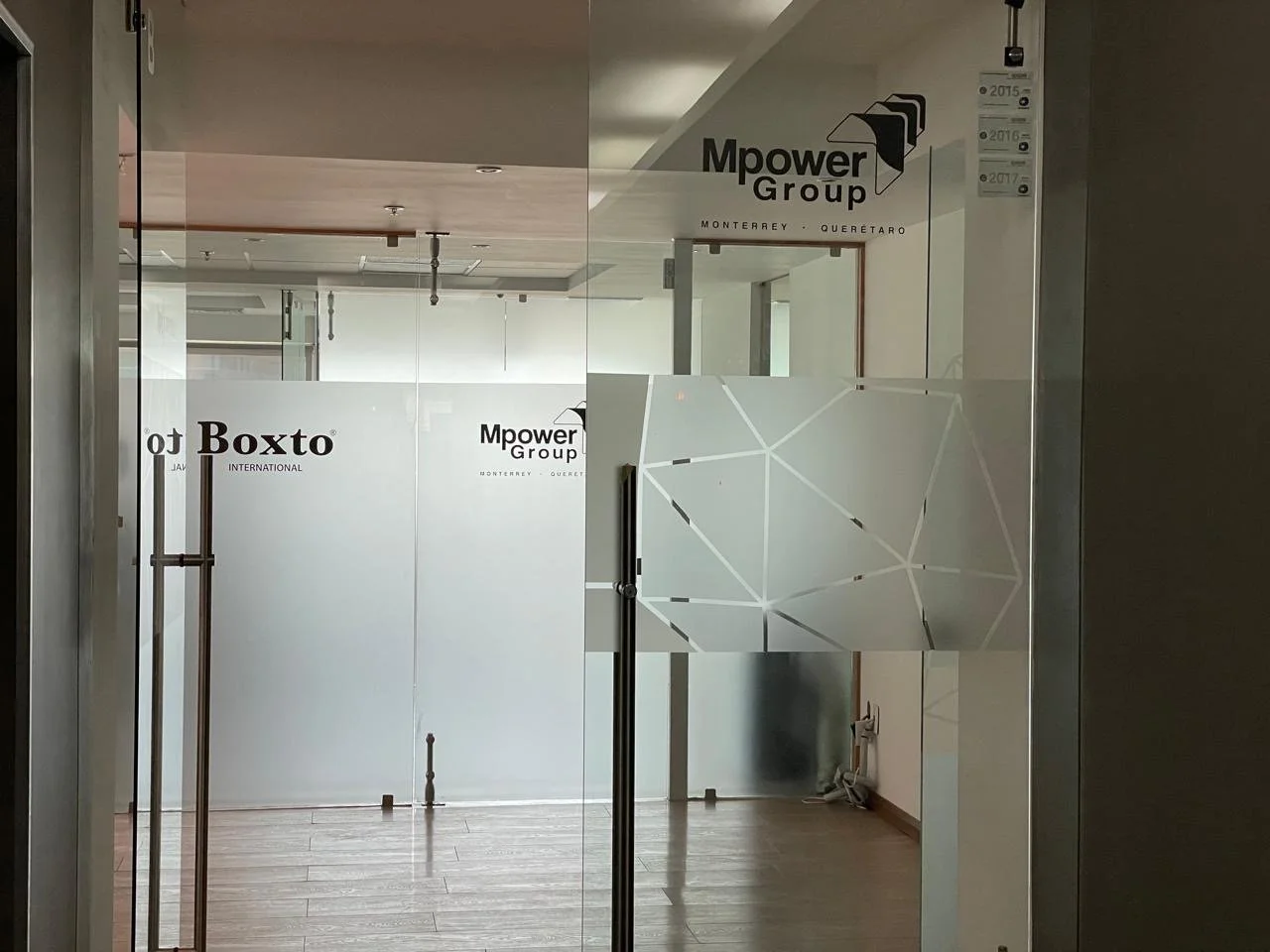 View through glass doors showing office interior with signs for Boxto International and Mpower Group, with wooden flooring and partial view of the ceiling and walls.